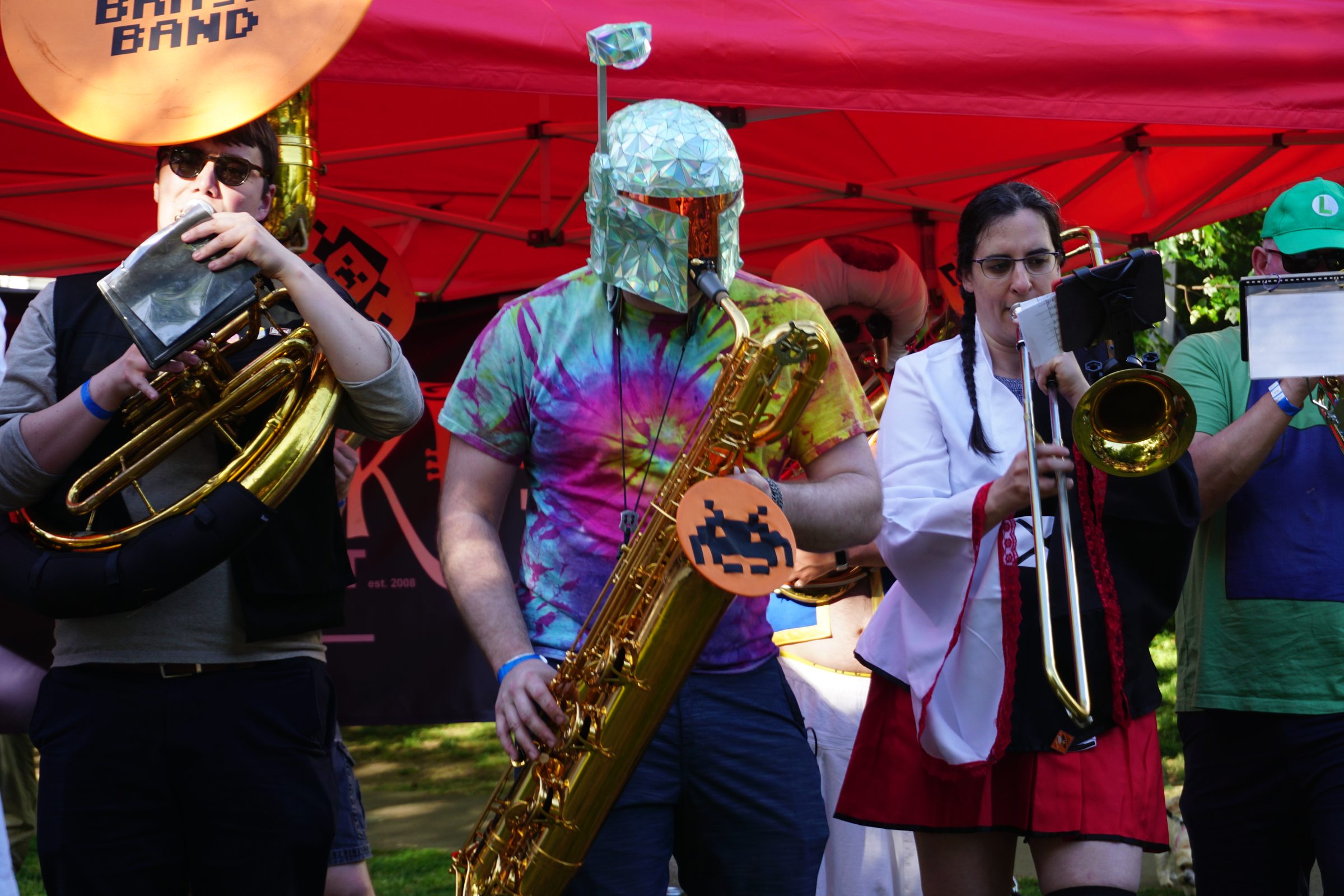 Wearing the dichroic helmet on baritone saxophone with the brass band under a red canopy.