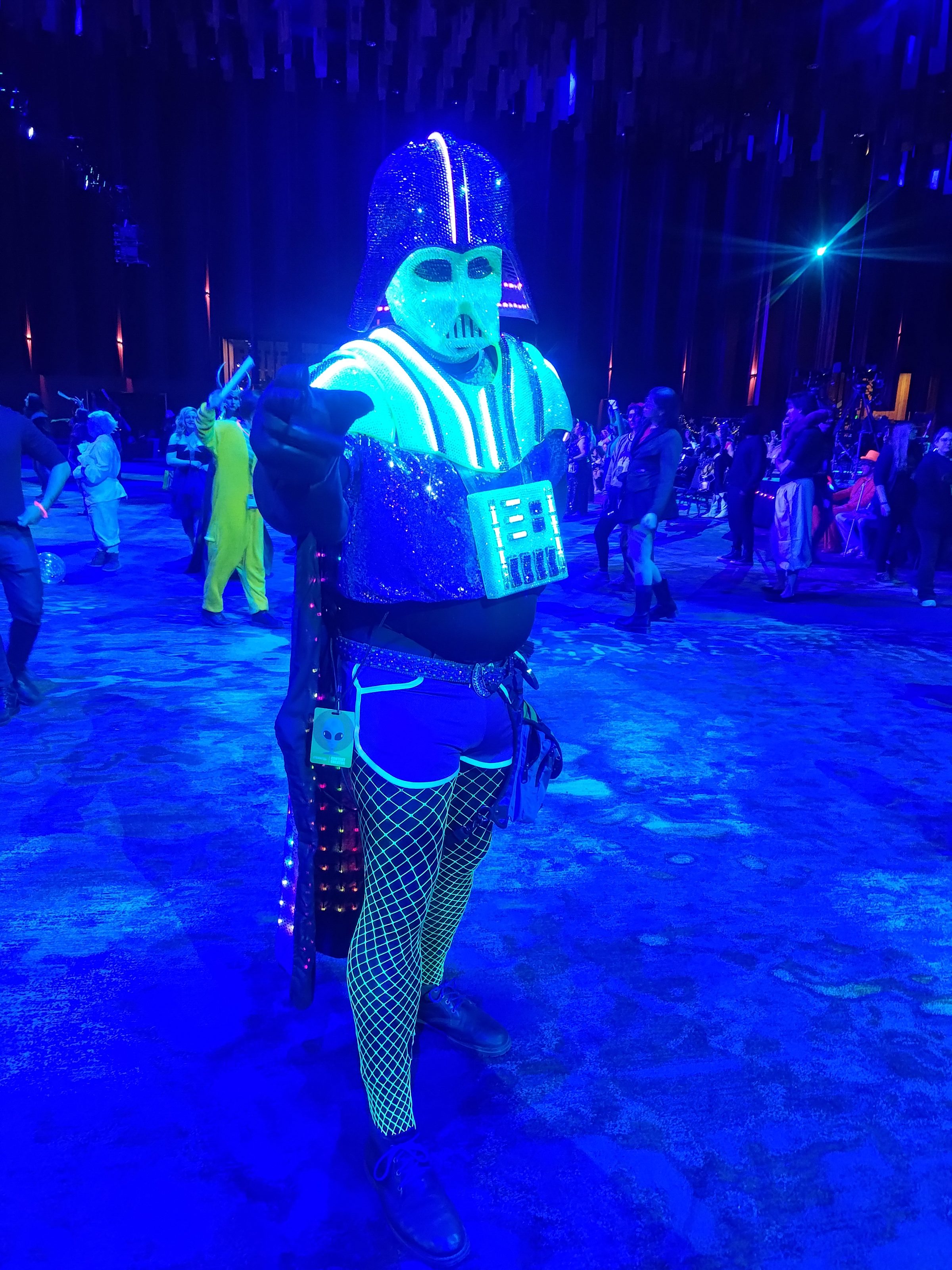 The Darth Daddy costume on a blue-lit dance floor, its chest and helmet traced in glowing white light.