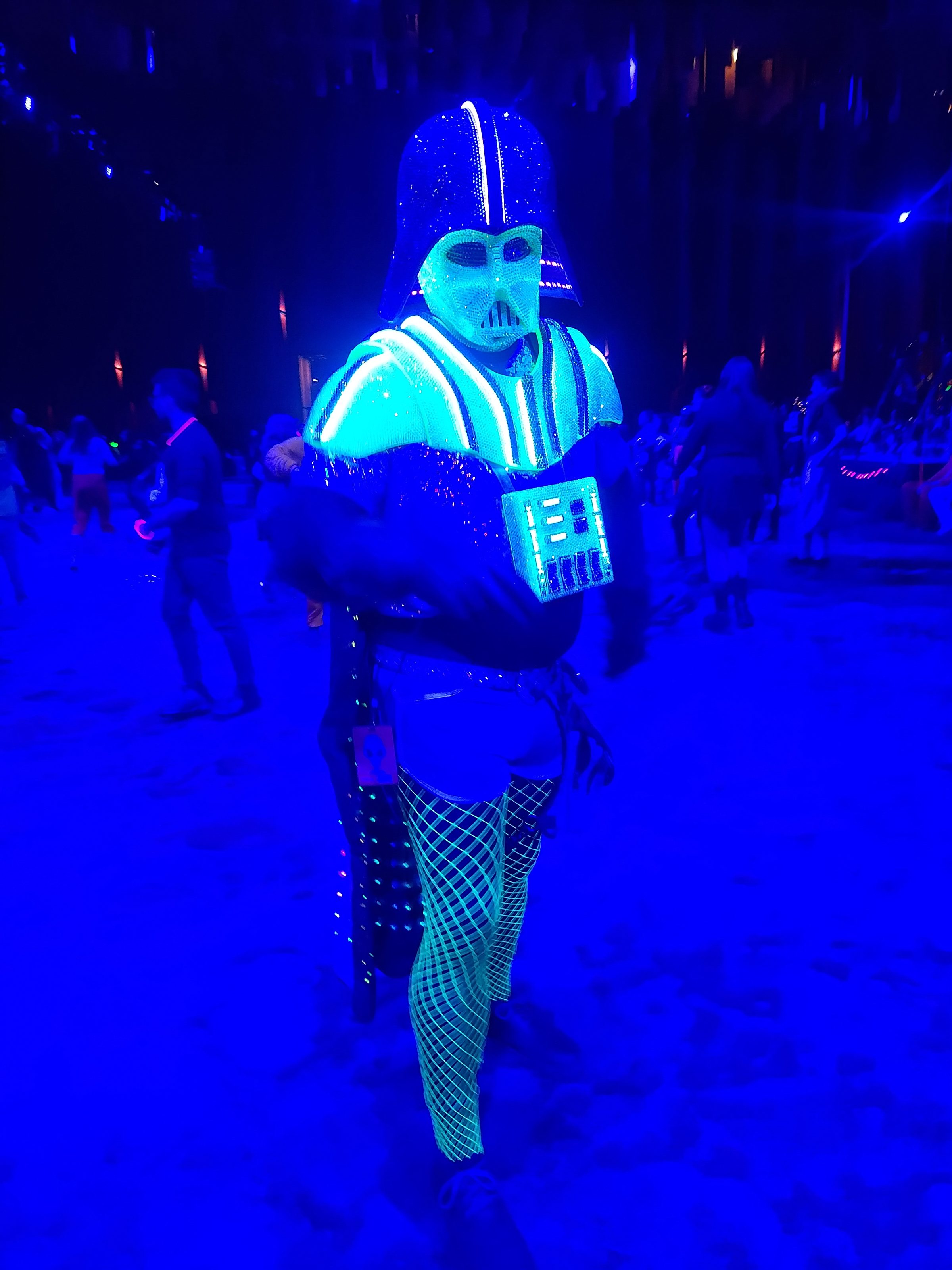 The Darth Daddy costume moving through a blue-lit crowd, EL wire glowing along the armour.