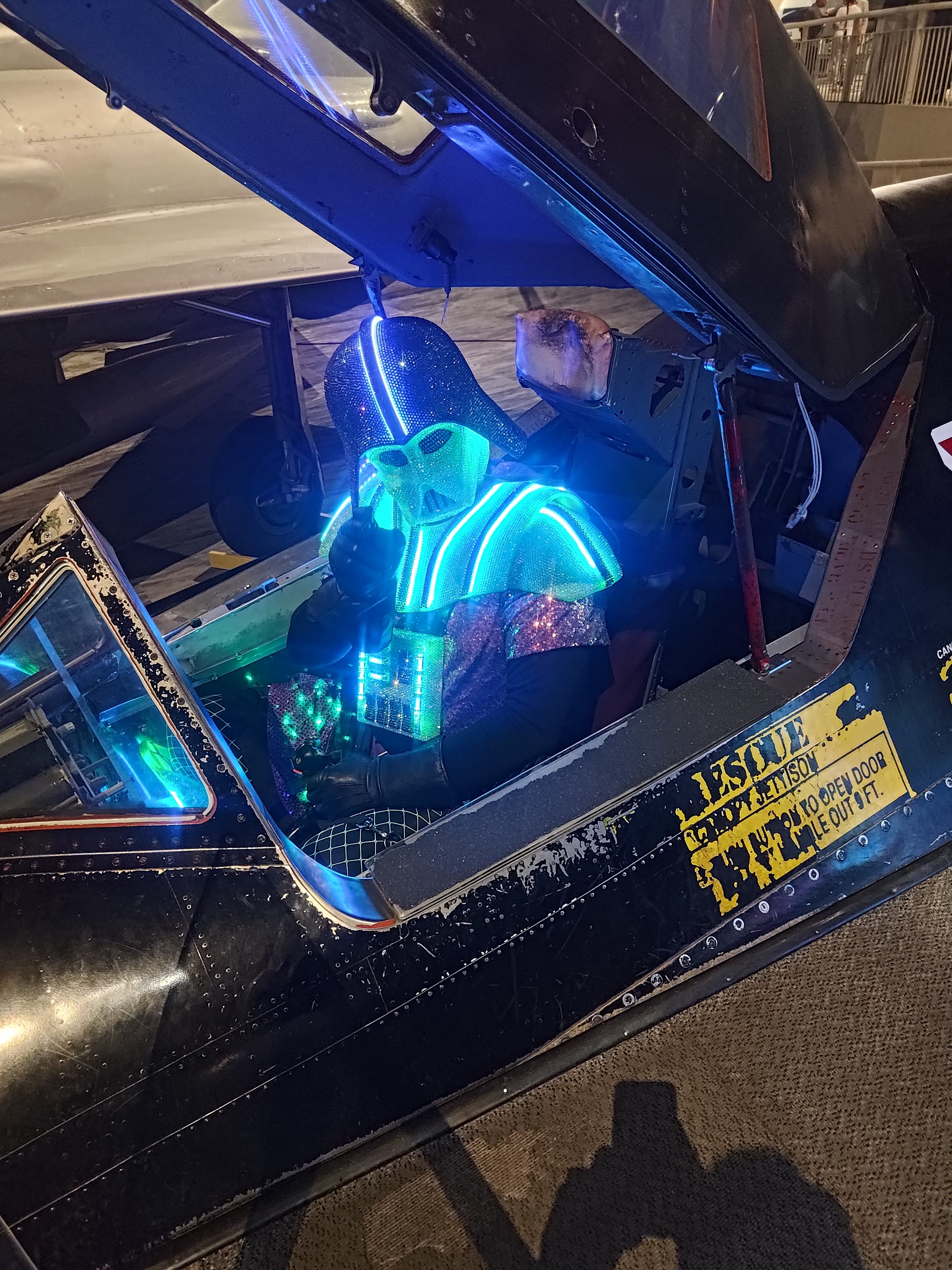 The Darth Daddy costume seated in an open aircraft cockpit, glowing against the dark hangar.