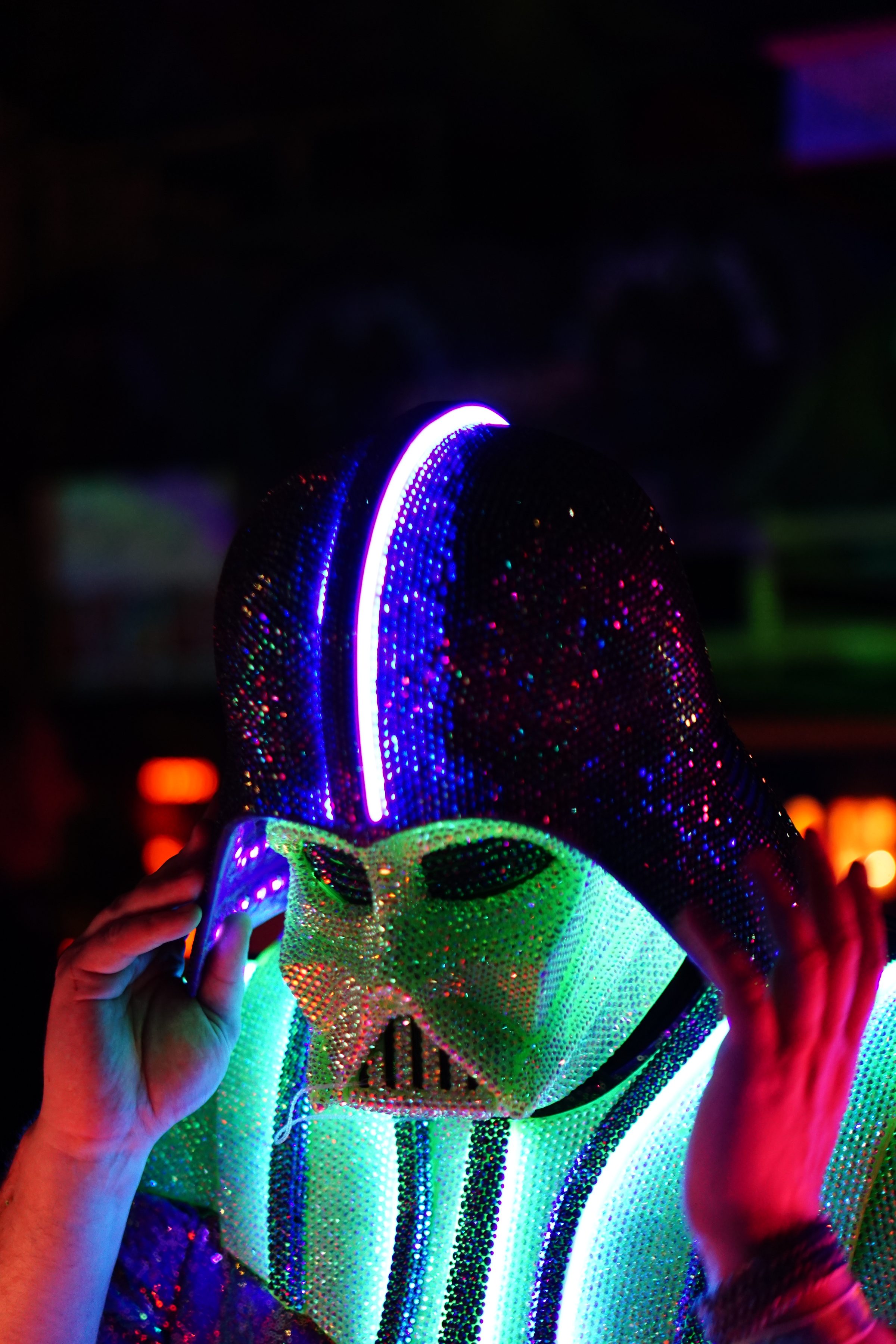 The Darth Daddy helmet lit magenta and green, gloved hands raised to the mask.