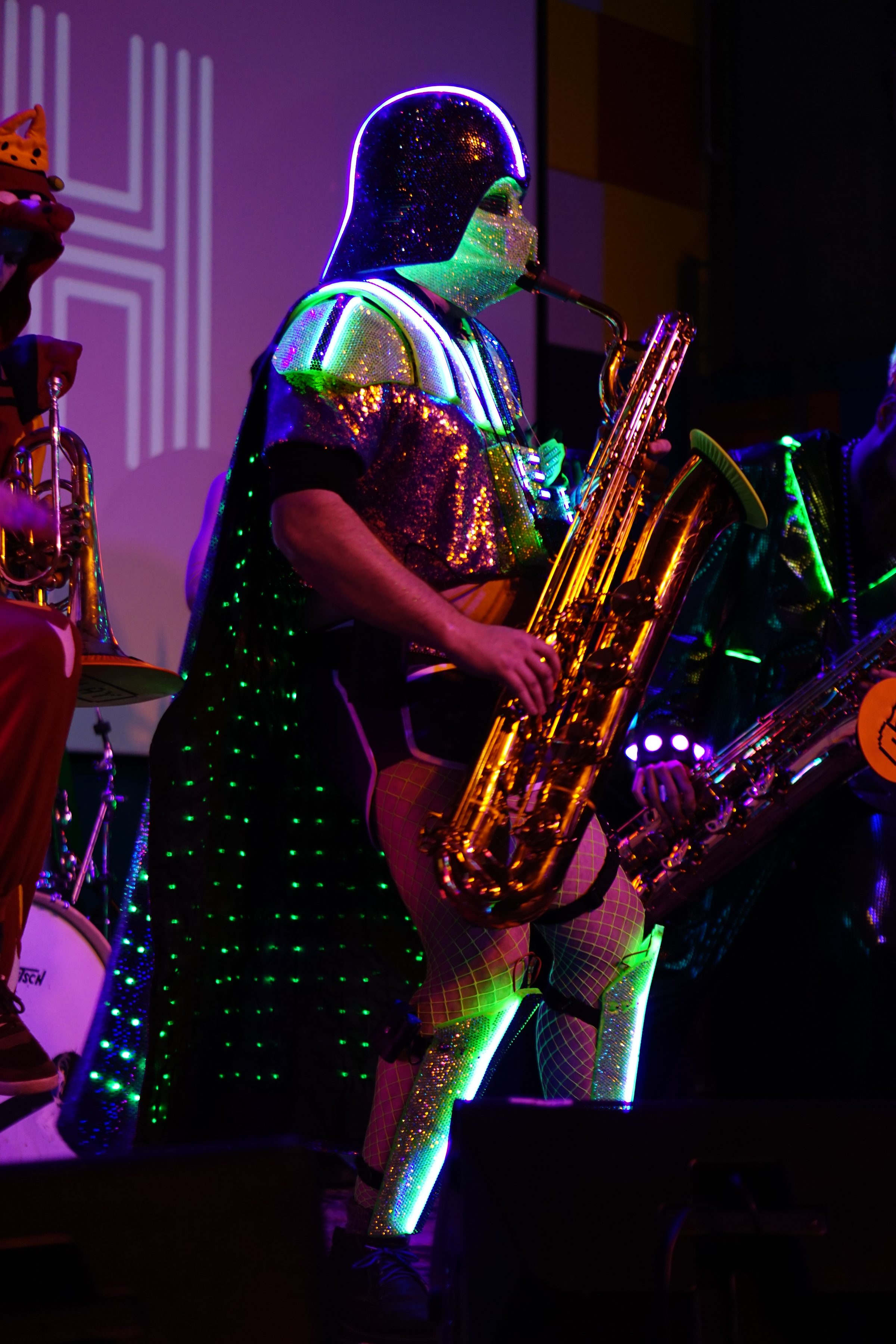 Playing baritone saxophone on stage in the Darth Daddy costume, cape and helmet glowing green.