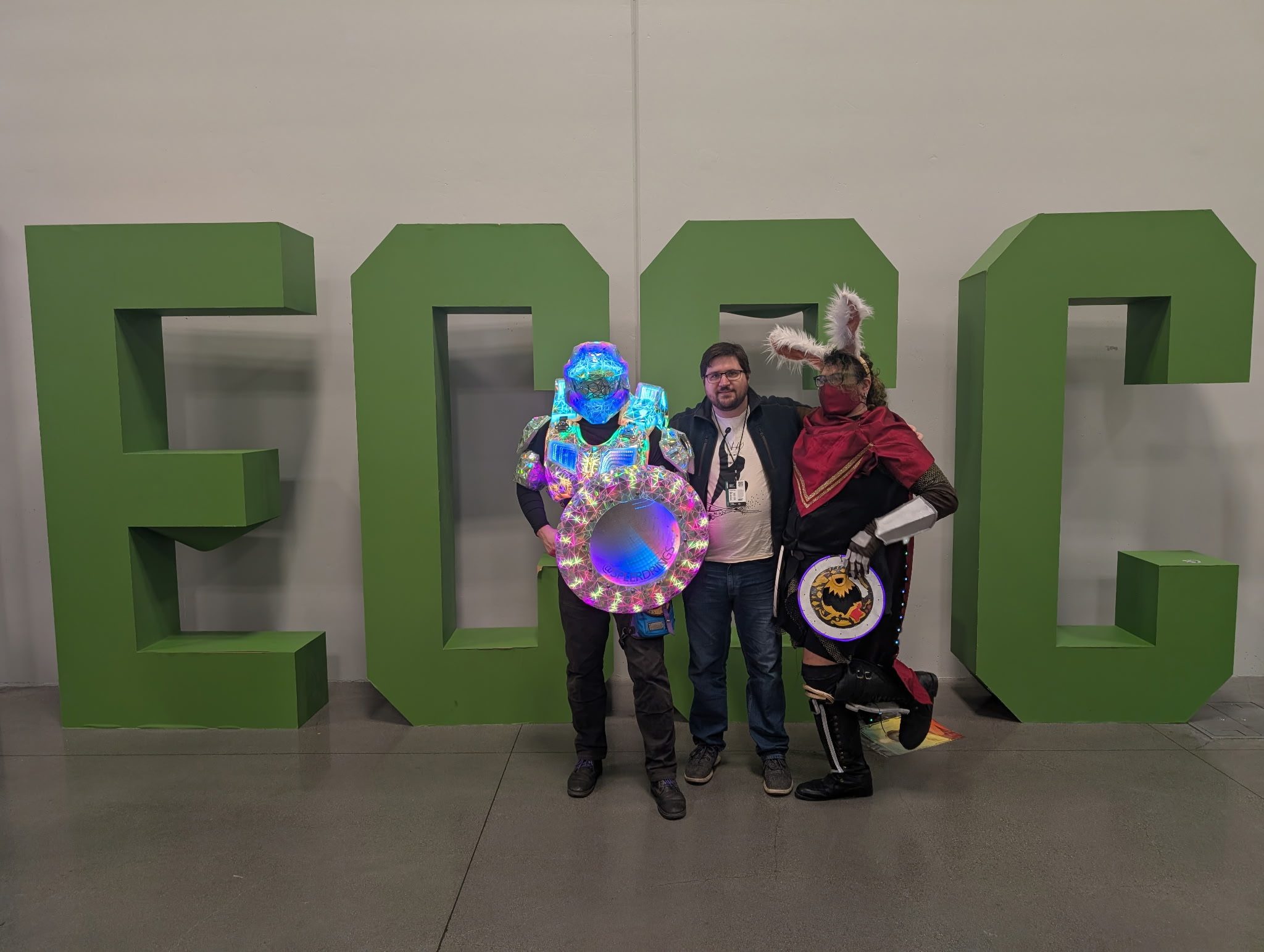 Standing with two other cosplayers in front of large green ECCC letters, holding the lit shield.