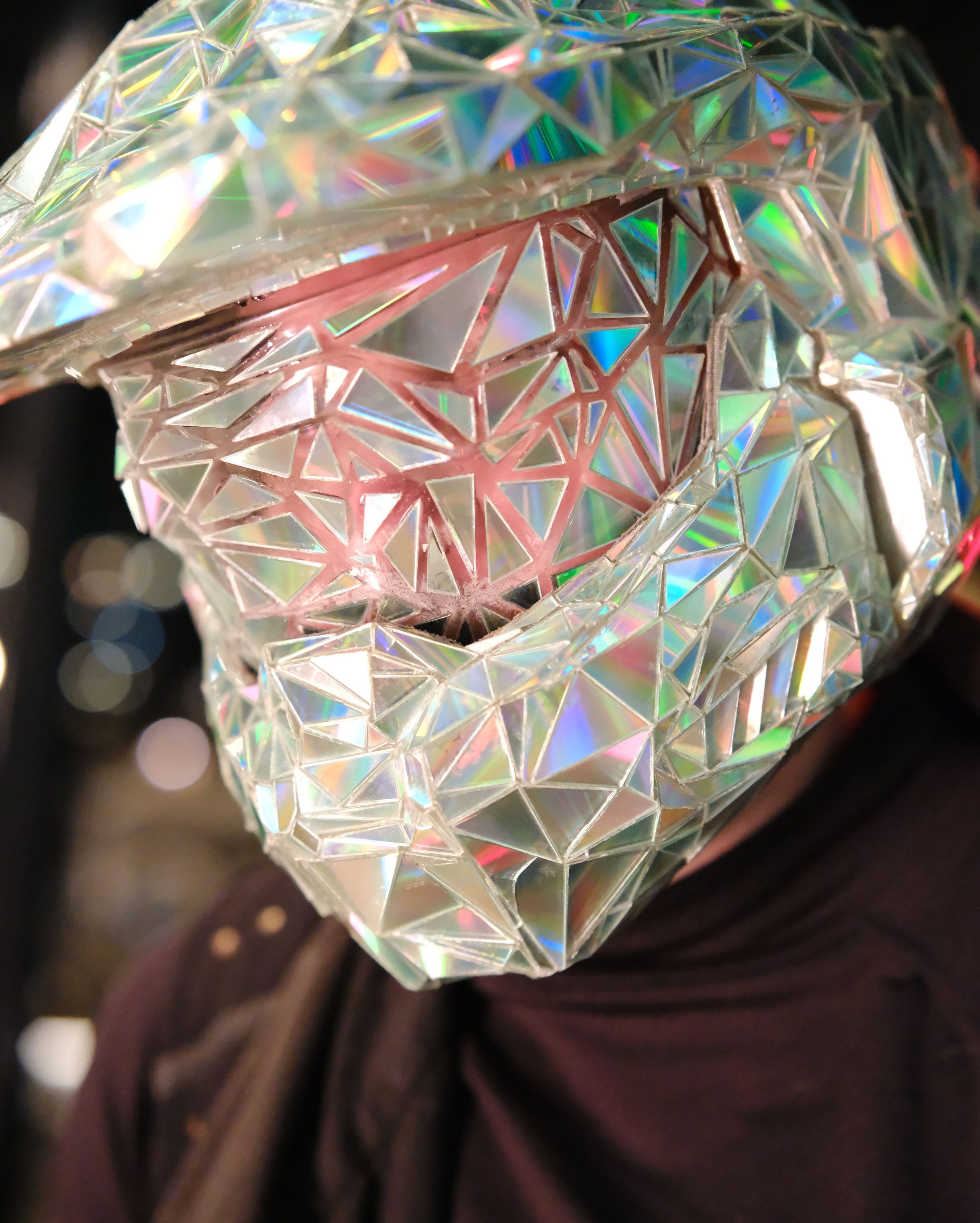 The faceted mirror helmet up close, its dichroic panels splitting the light into greens and pinks.
