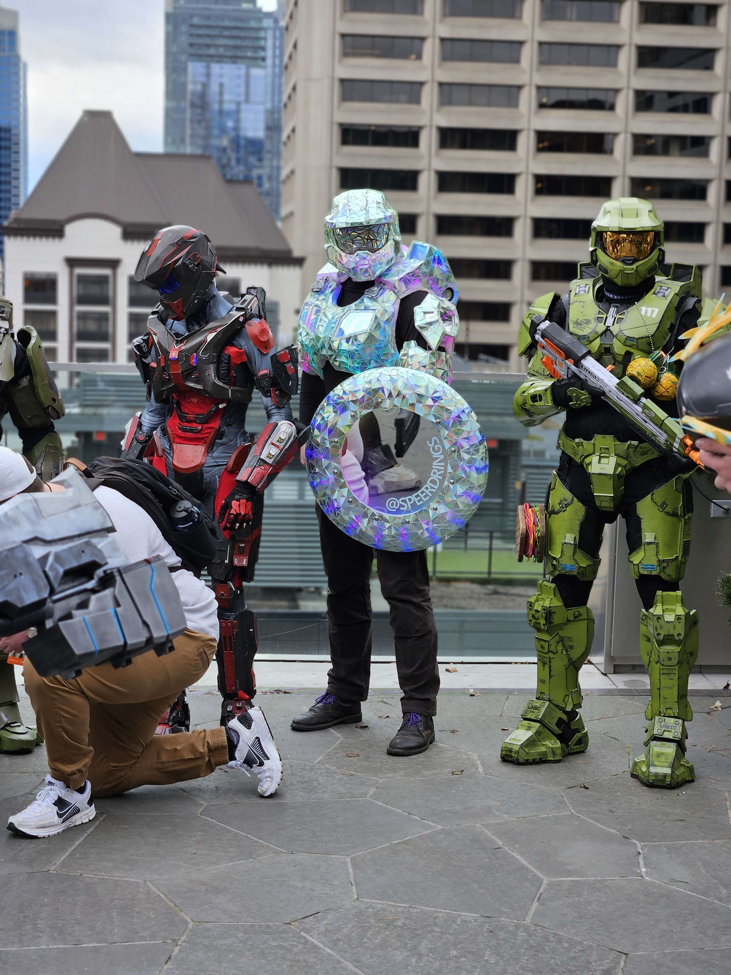 Disco Chief and the faceted shield among a line of Spartan cosplayers on a rooftop above the city.
