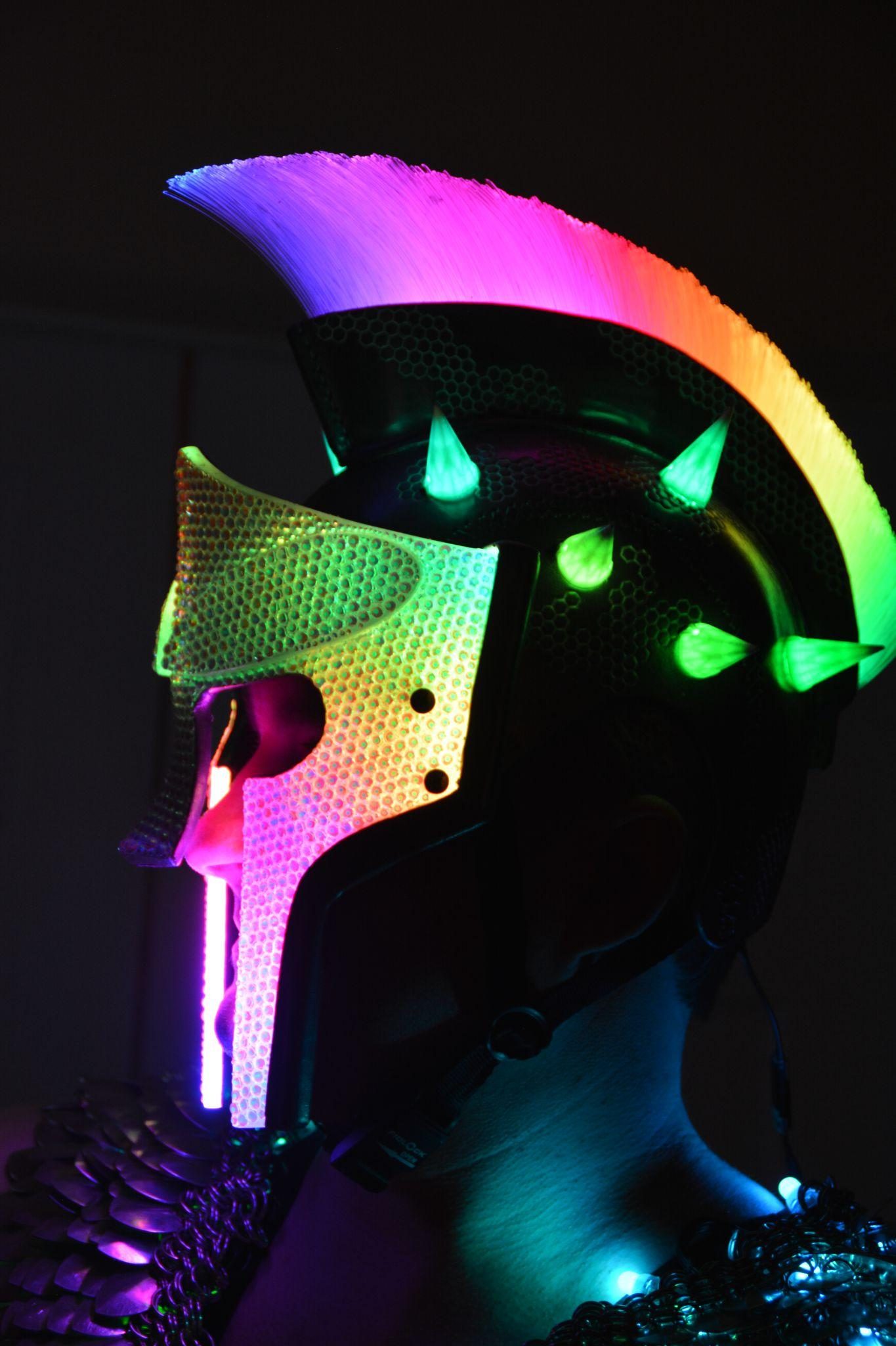 The finished helmet on a stand in the dark, its fibre-optic mohawk washed in rainbow light and its horns glowing green.