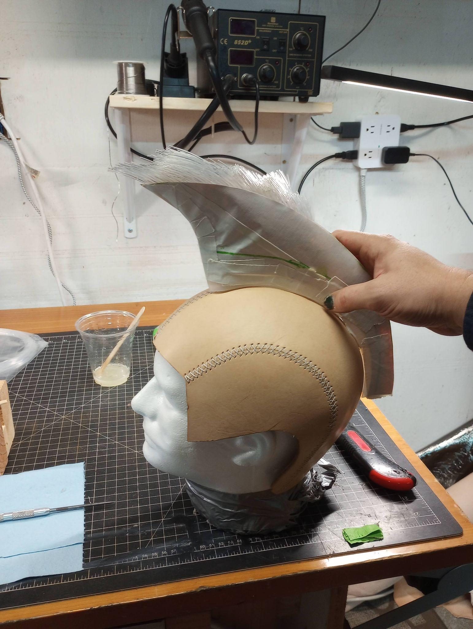 The leather helmet on a foam head form at the bench while a fibre-optic mohawk channel is fitted to its crown.