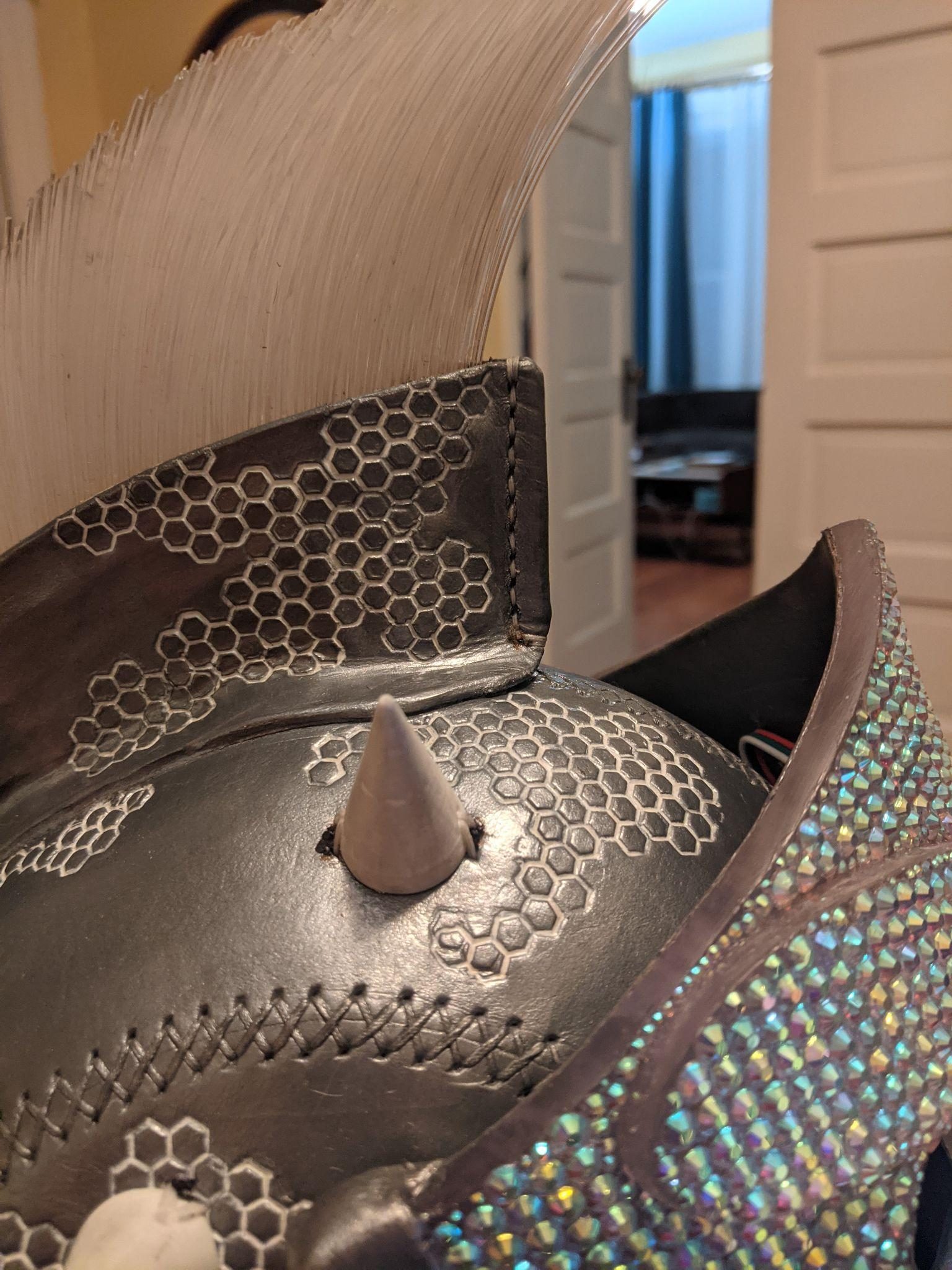 Close-up of the helmet crown: hexagon stamping across black leather, one printed horn, and the rhinestoned edge of the face plate.