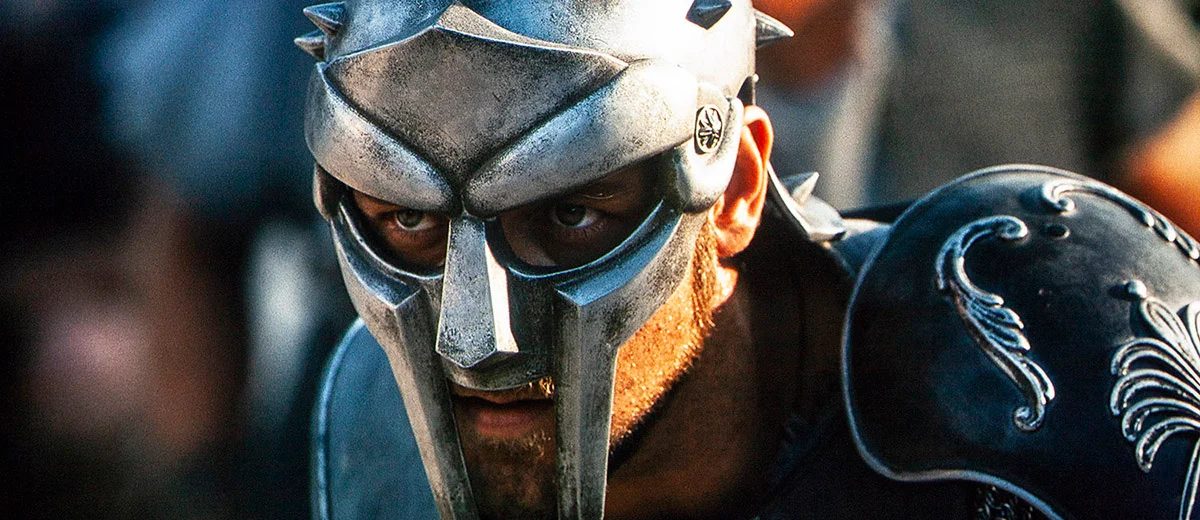 Film still of Maximus in a spiked Roman helmet and pauldron, eyes shadowed behind the visor.