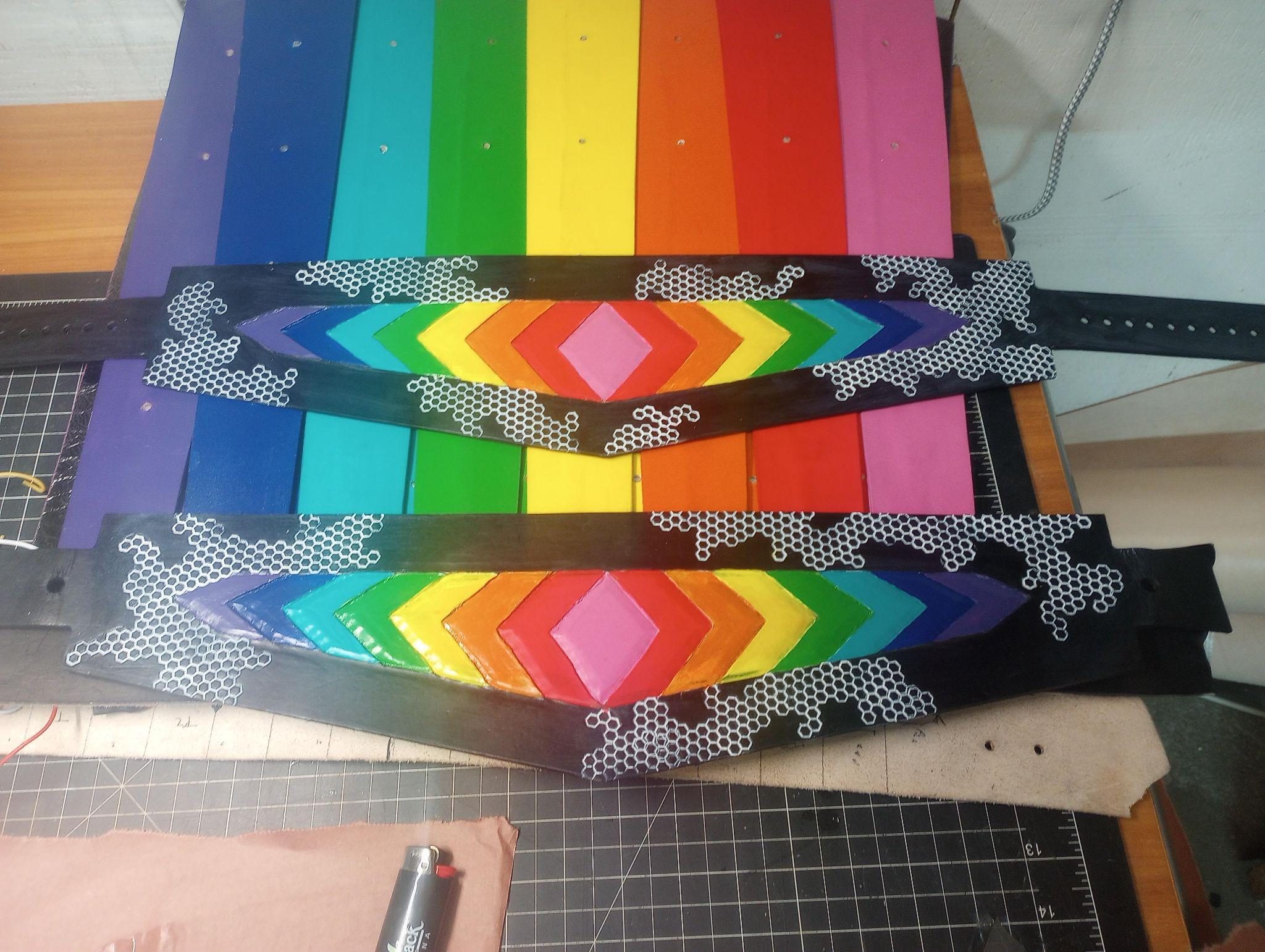 Two hexagon-stamped leather belts painted with rainbow chevrons, resting across the painted kilt panels.