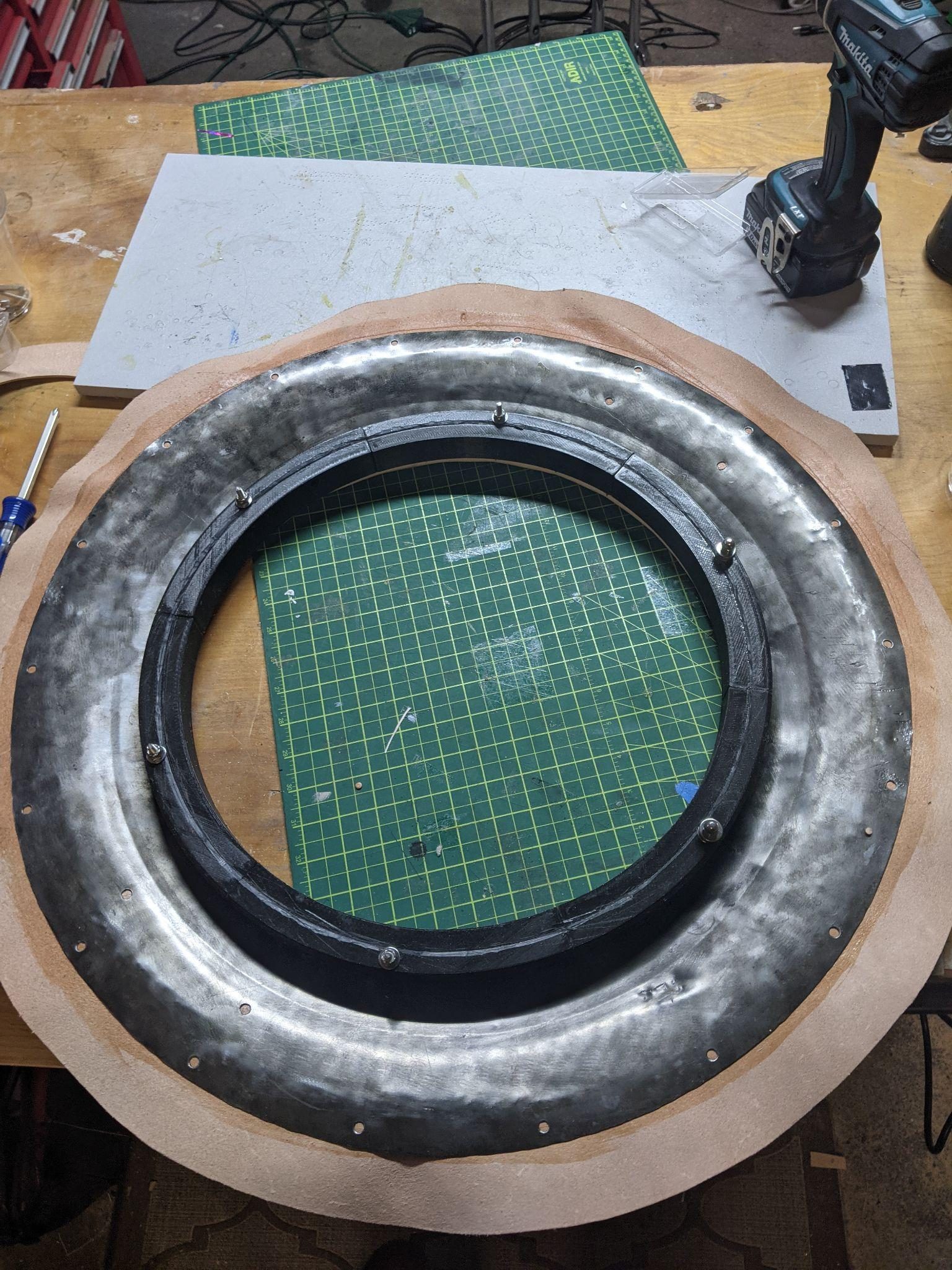 The shield stripped to bare steel on the workbench, its printed black ring sections bolted into the leather-edged rim.