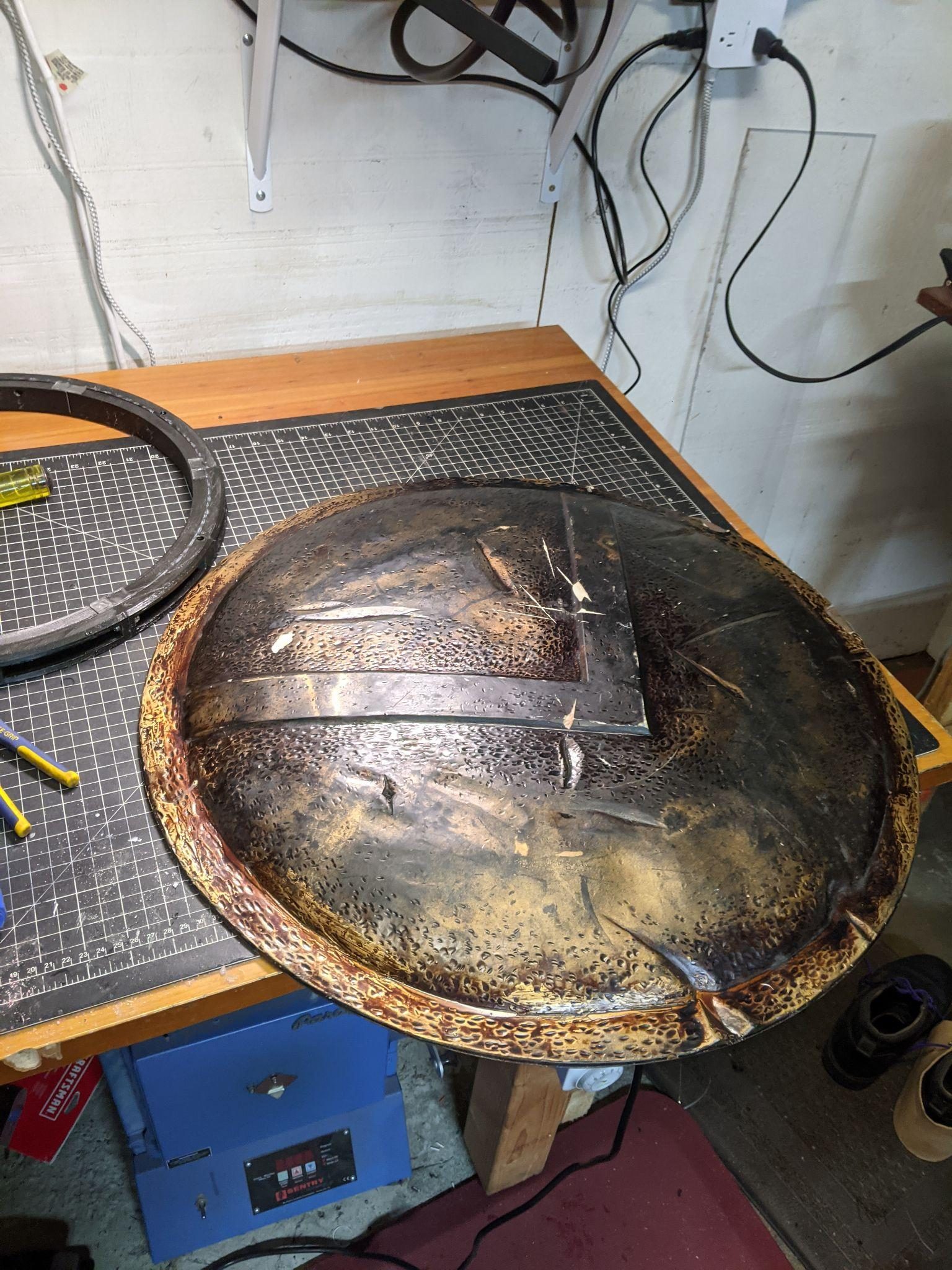 The shield face down on the bench, its hexagon-stamped leather scorched and burnished, the printed ring waiting alongside.