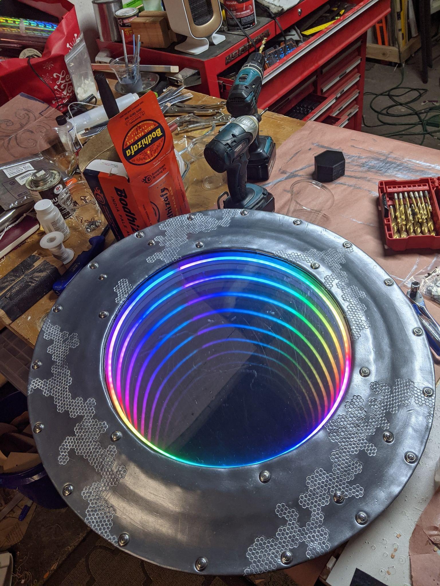 The finished shield on the bench with its infinity mirror lit, concentric rainbow rings receding into the centre.