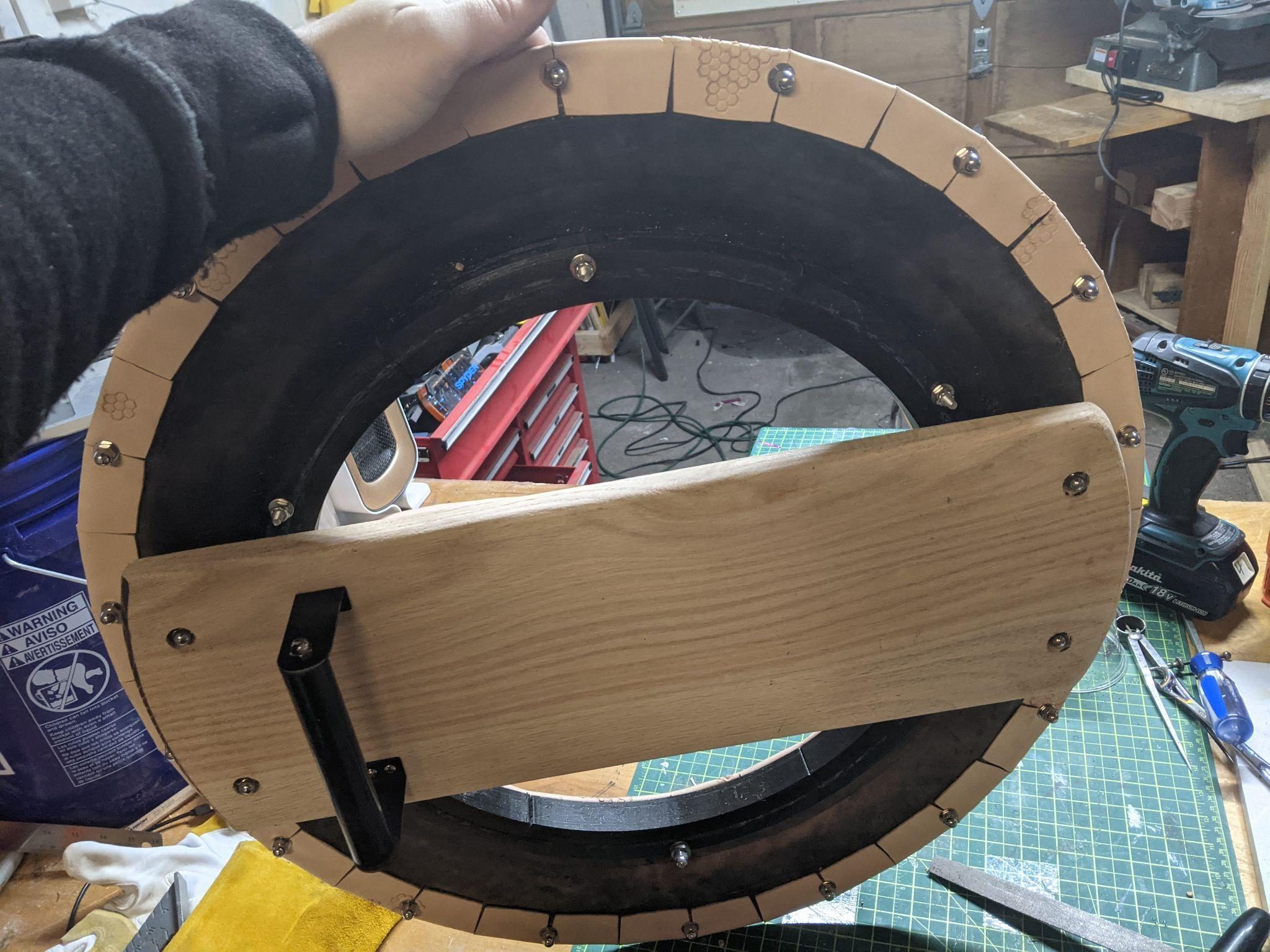 Holding the back of the shield in the shop, showing the oak arm bracket standing off the mirror assembly on black offsets.