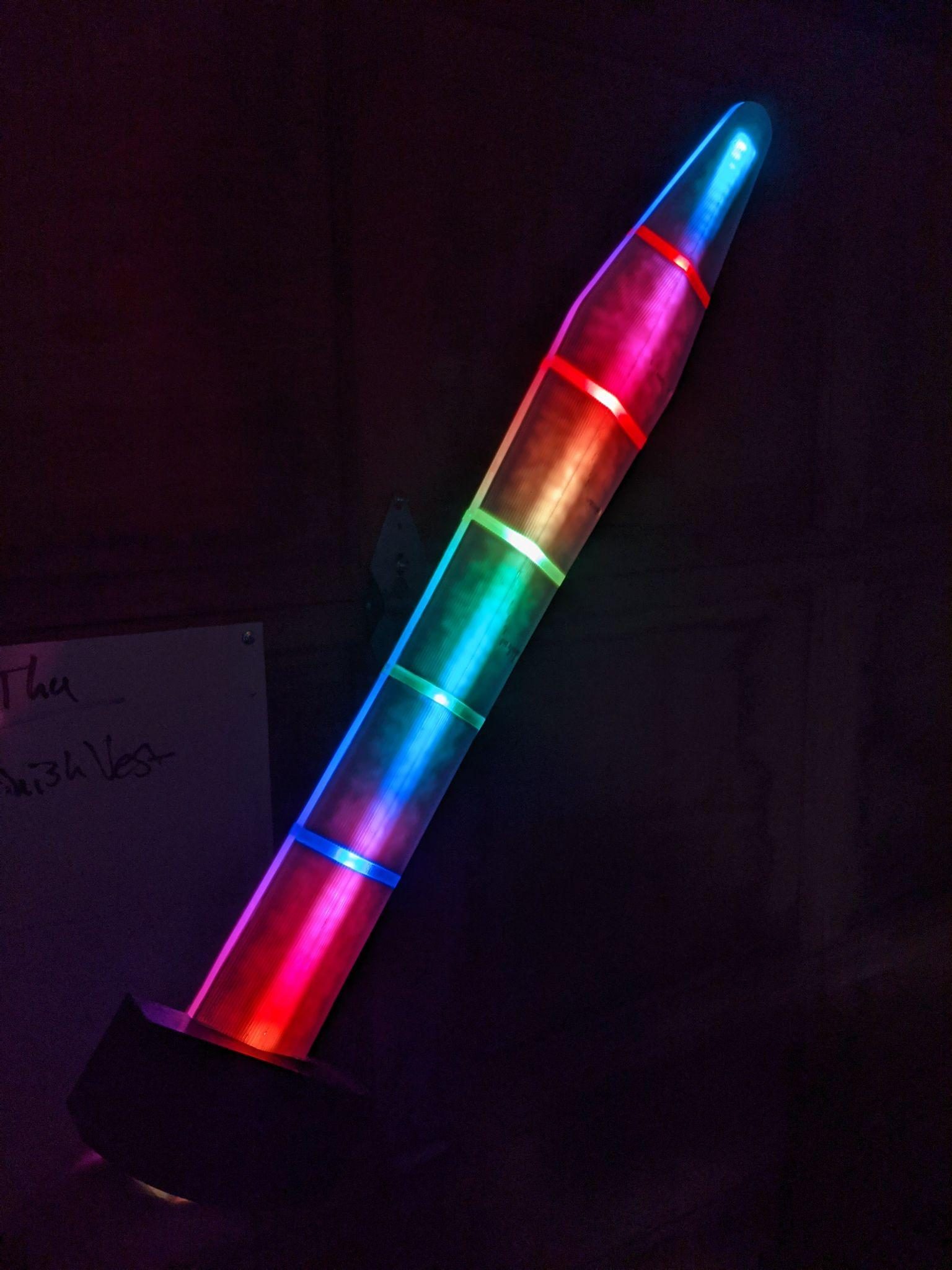 The sword lit in a dark room, colour running the length of the blade from magenta at the hilt to blue at the tip.
