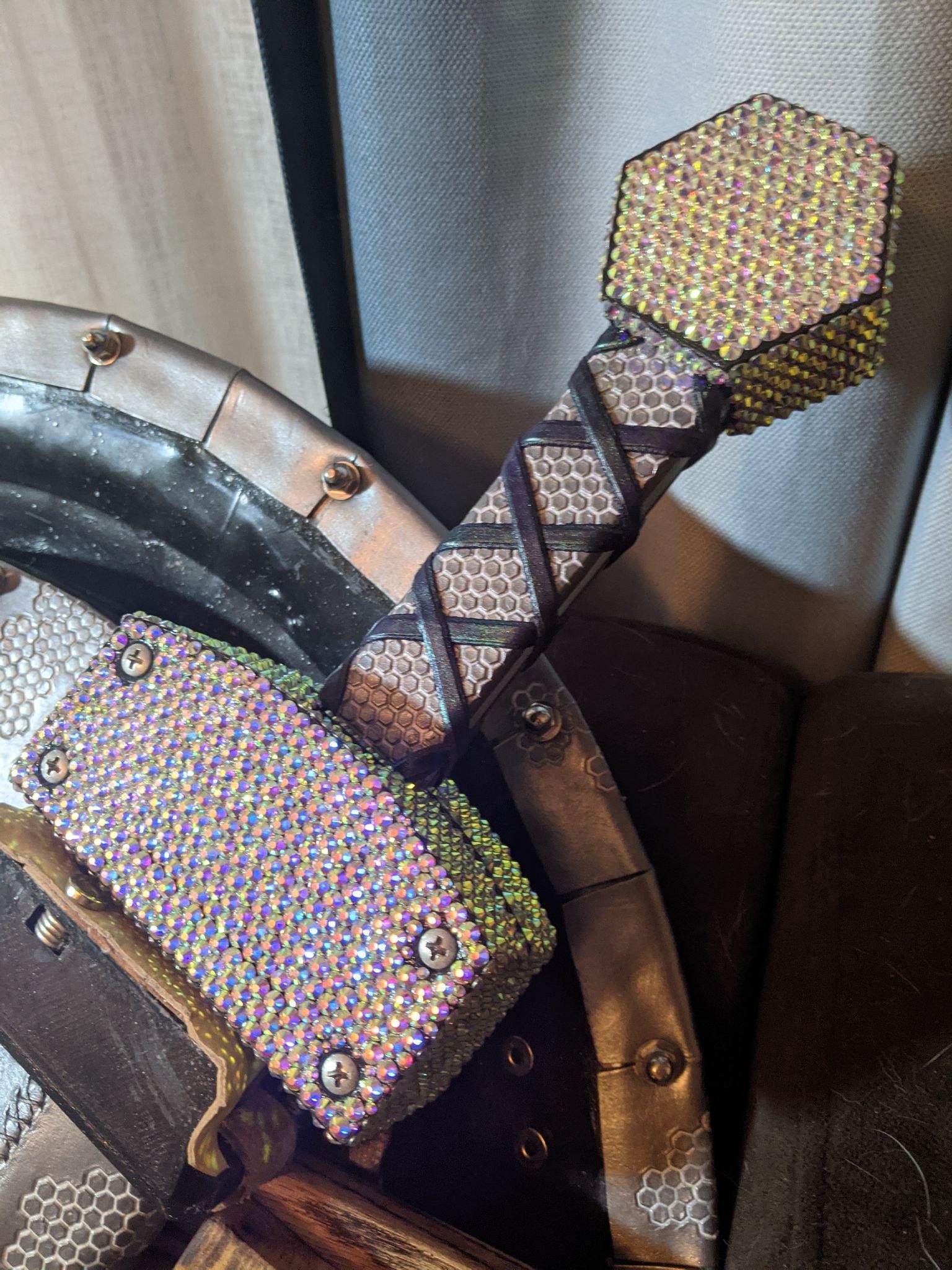 Close-up of the sword hilt: a rhinestoned hexagonal pommel and guard block above a cross-wrapped leather grip.