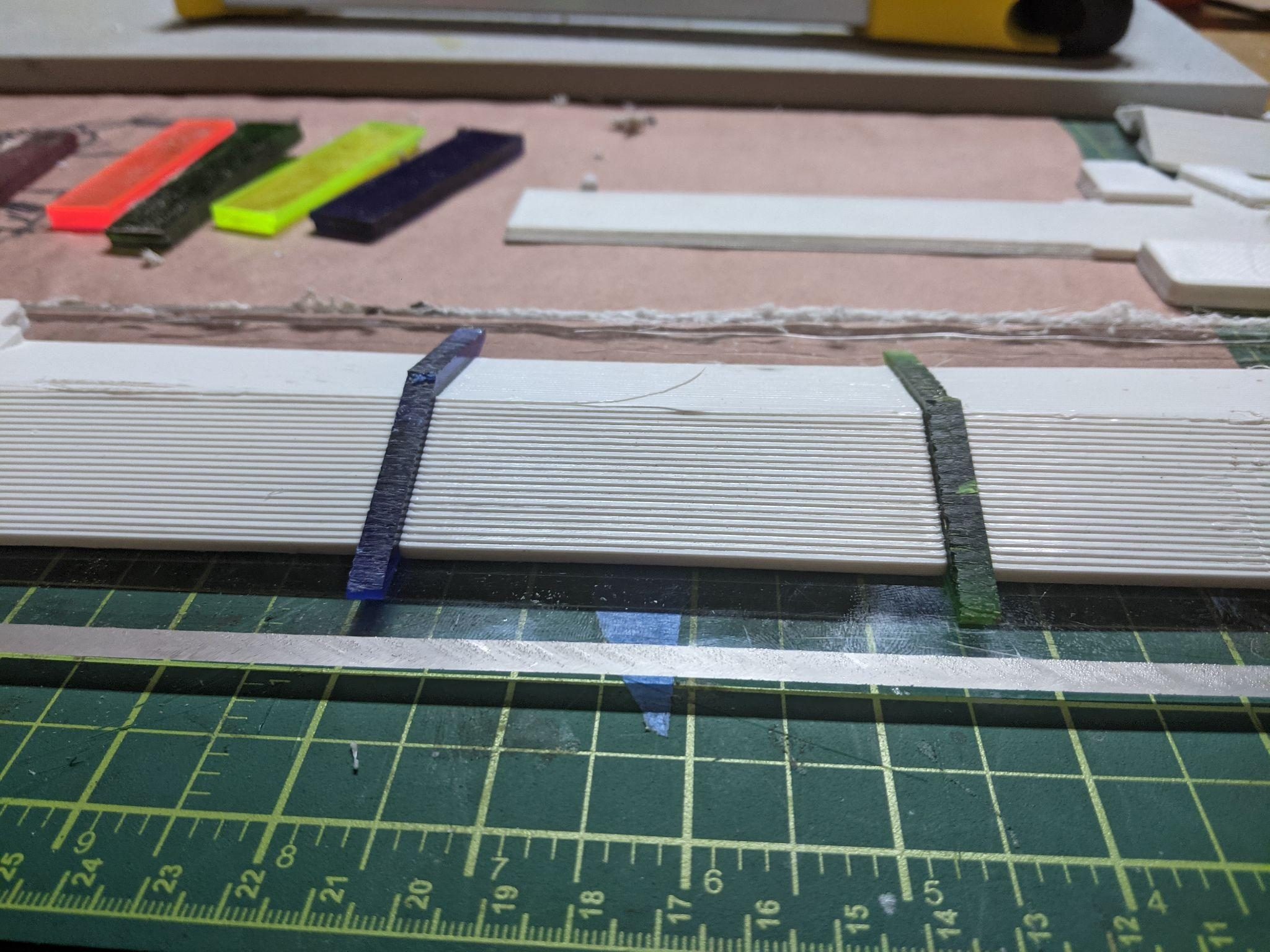 Two thin acrylic strips standing on edge in the channel between white printed blade panels during lamination.