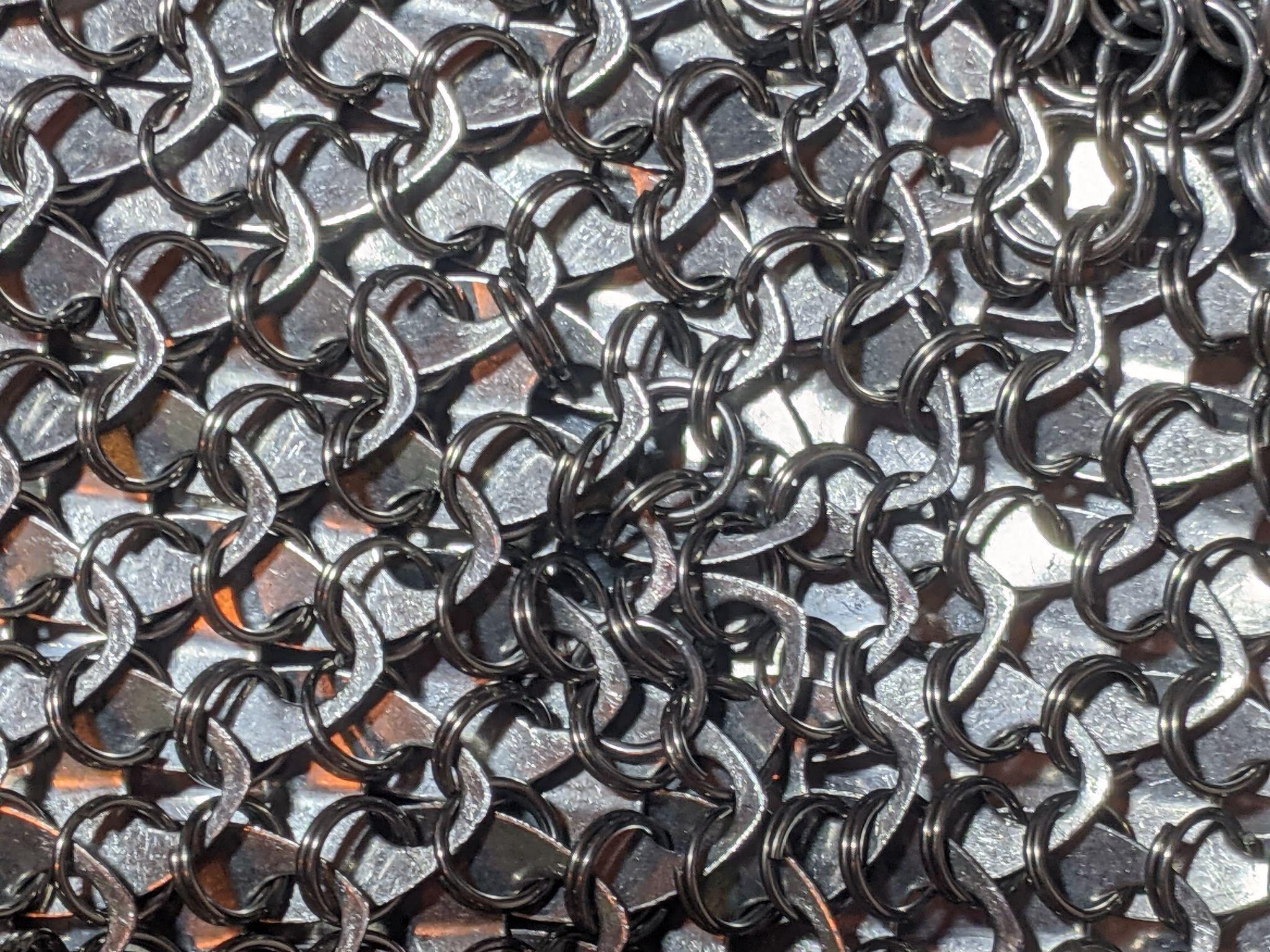 Extreme close-up of blackened kingsmaille, its rings woven tight over overlapping metal scales.