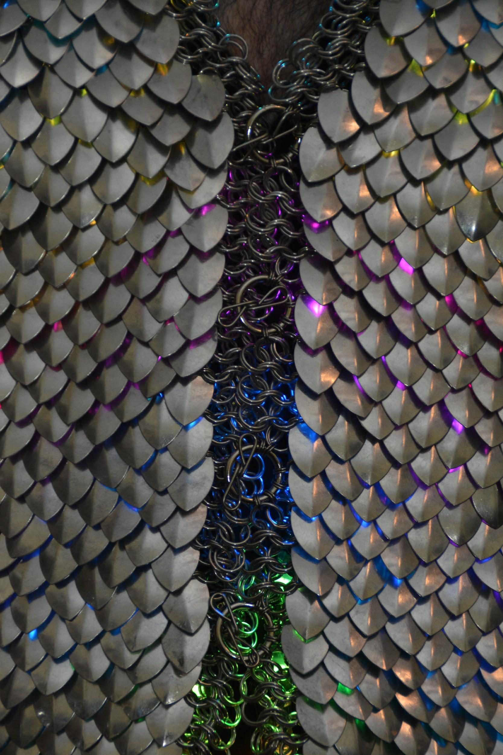 The scale maille vest closed at the chest, LED light glowing up through silver scales along a kingsmaille centre strip.