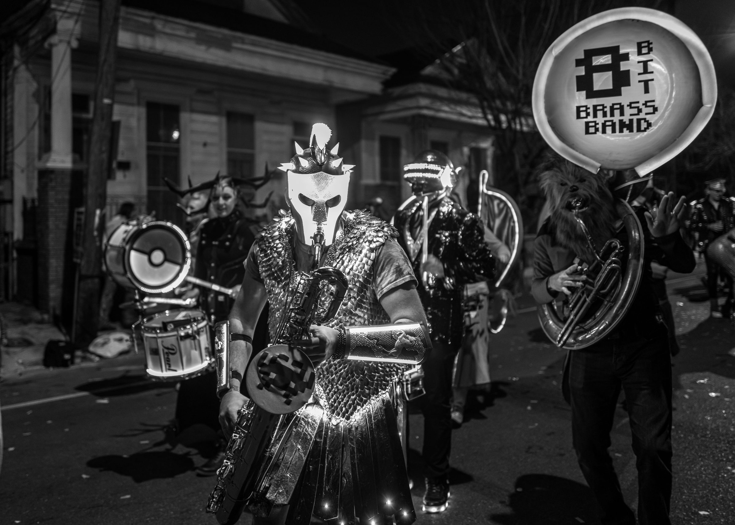 Black and white photograph of the 8-Bit Brass Band marching at night, the Russell Glow helmet among them.