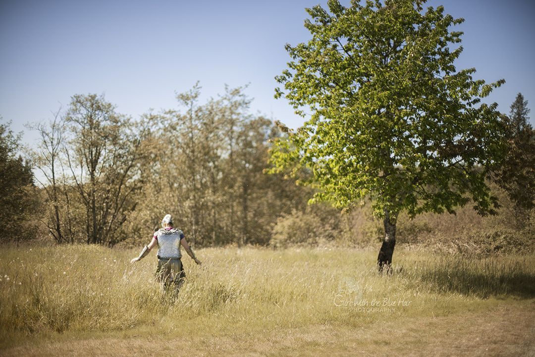 Wearing the costume seen from behind, walking away through tall dry grass toward a lone tree.