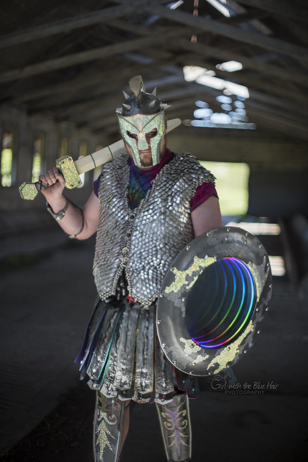 Standing in a barn with the sword on one shoulder and the lit shield held low.
