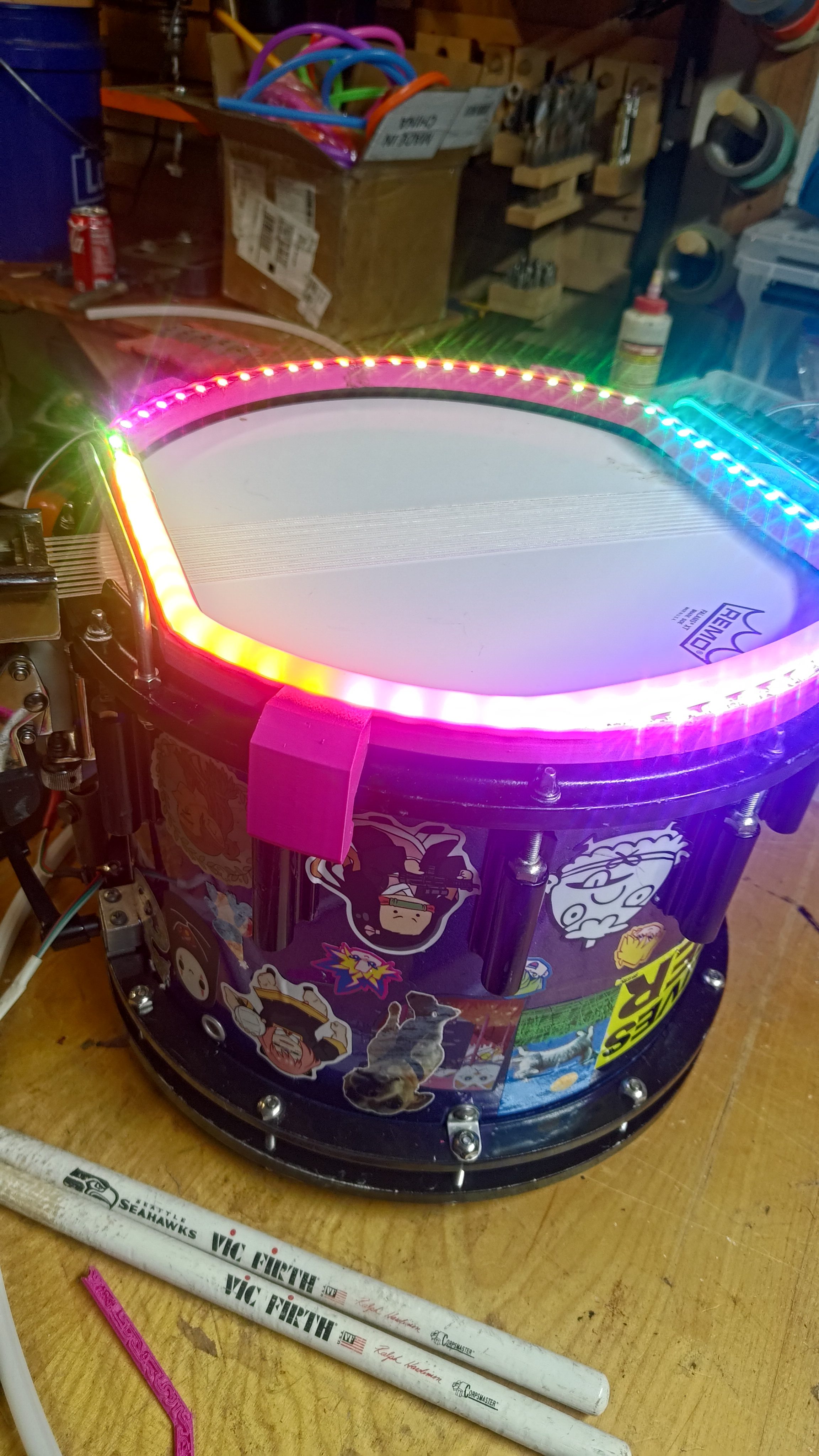 A snare drum ringed with rainbow LEDs on a workbench.