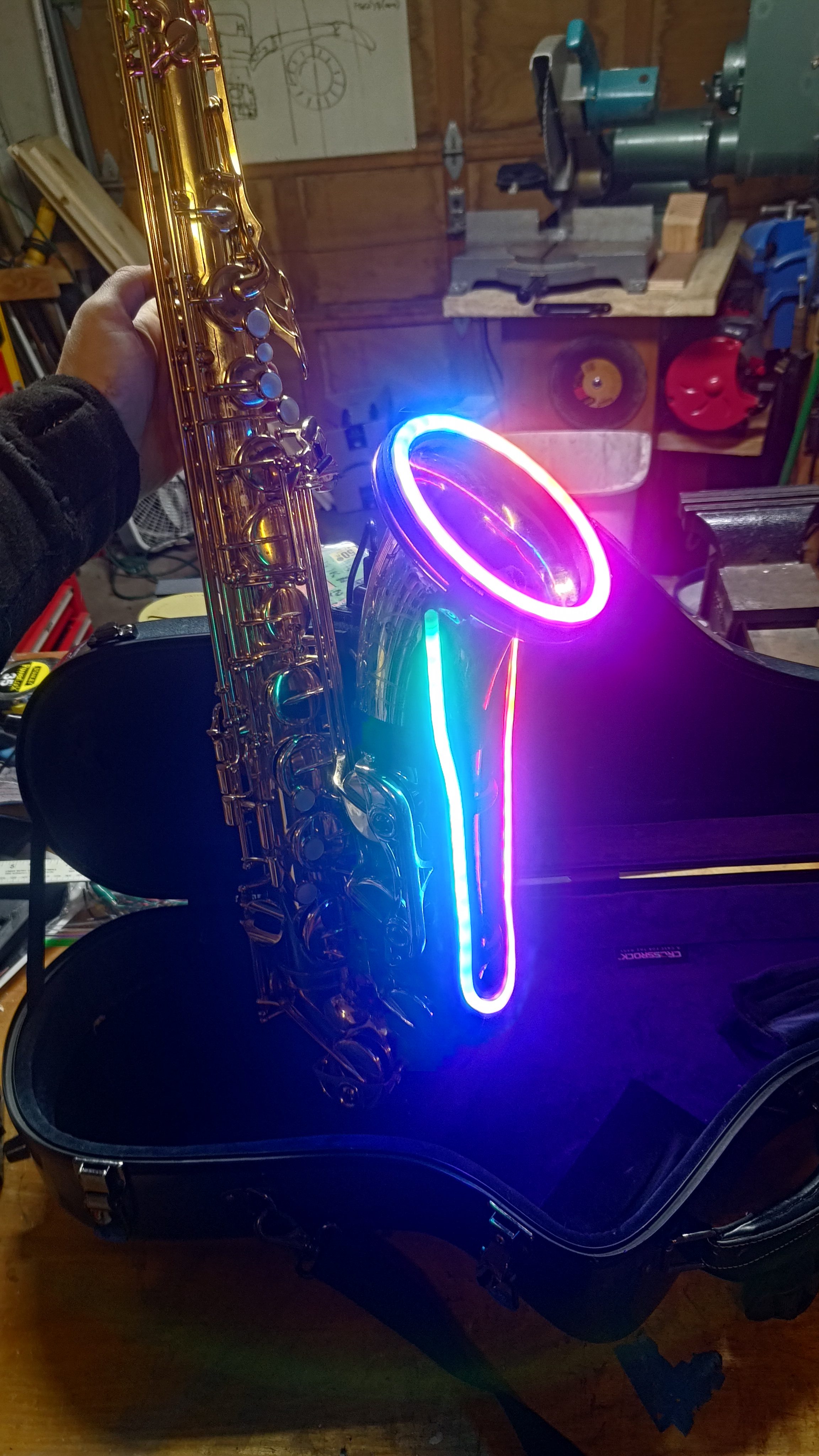 A saxophone with a magenta glowing ring and stem mounted beside its bell.