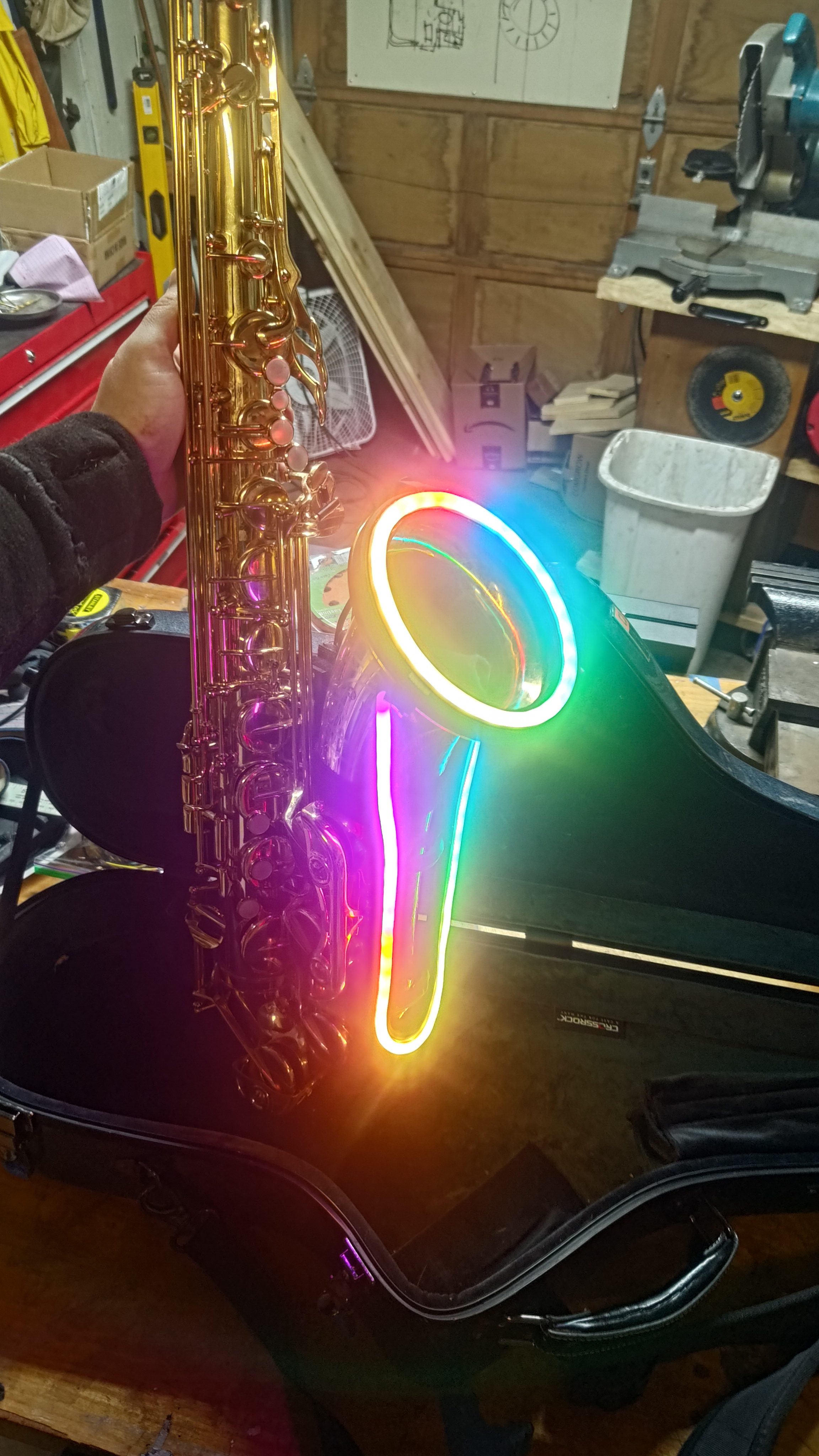 A saxophone with a white and rainbow lit ankh-shaped fixture.
