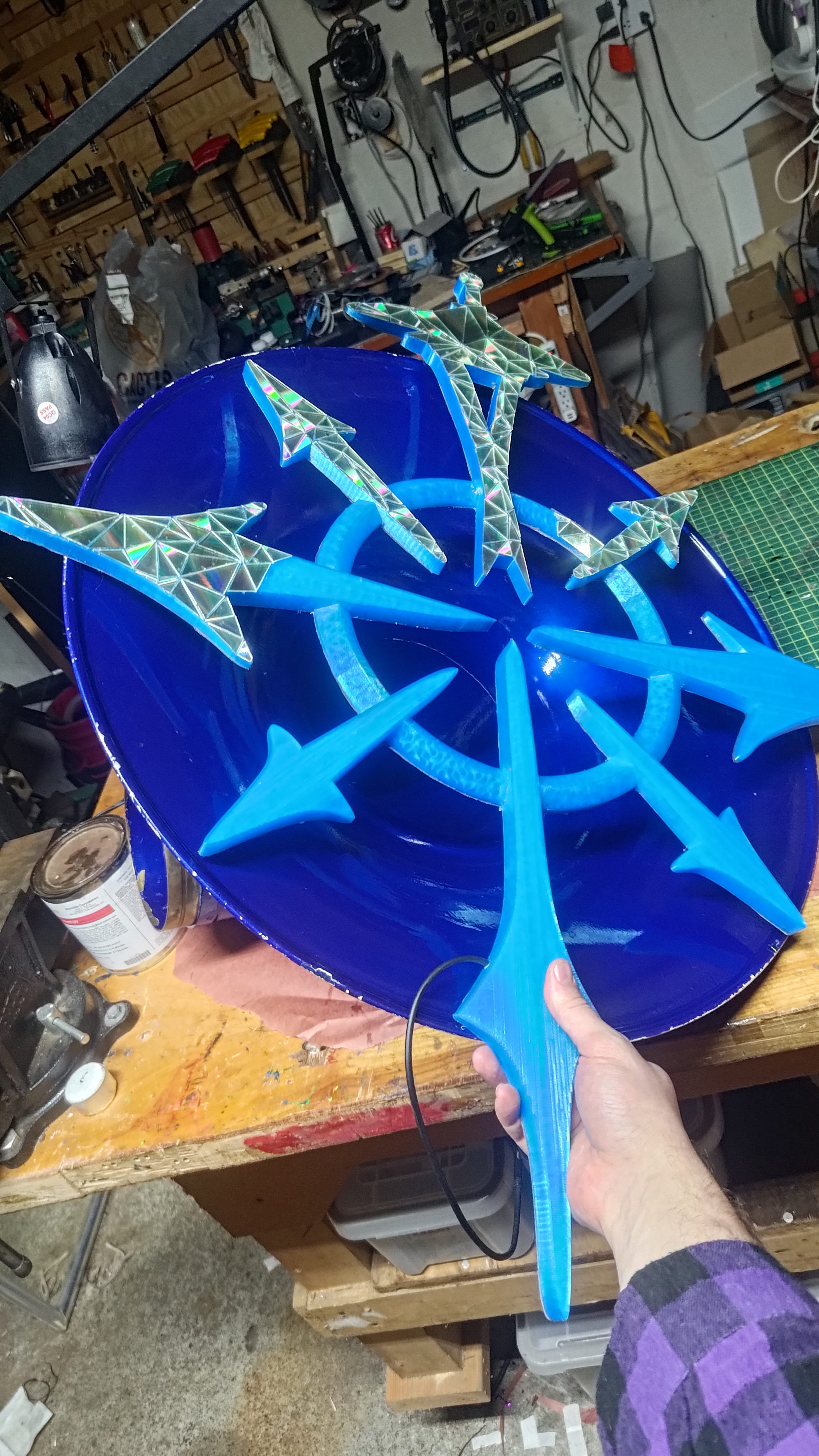 A blue disc bearing a chaos star of arrows, held up in the workshop.