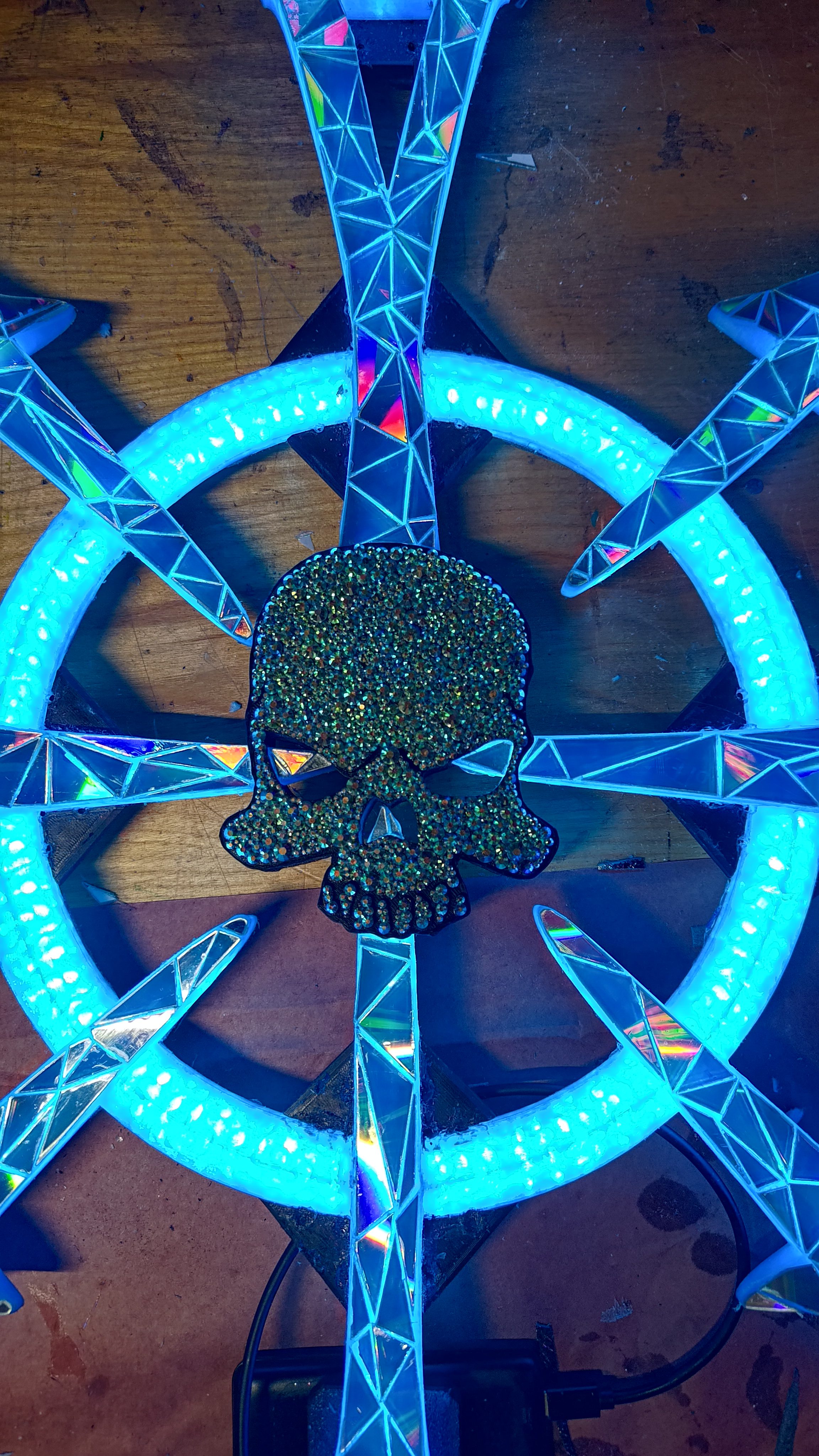 A ship's wheel fixture ringed with cyan LEDs around a glittered skull.