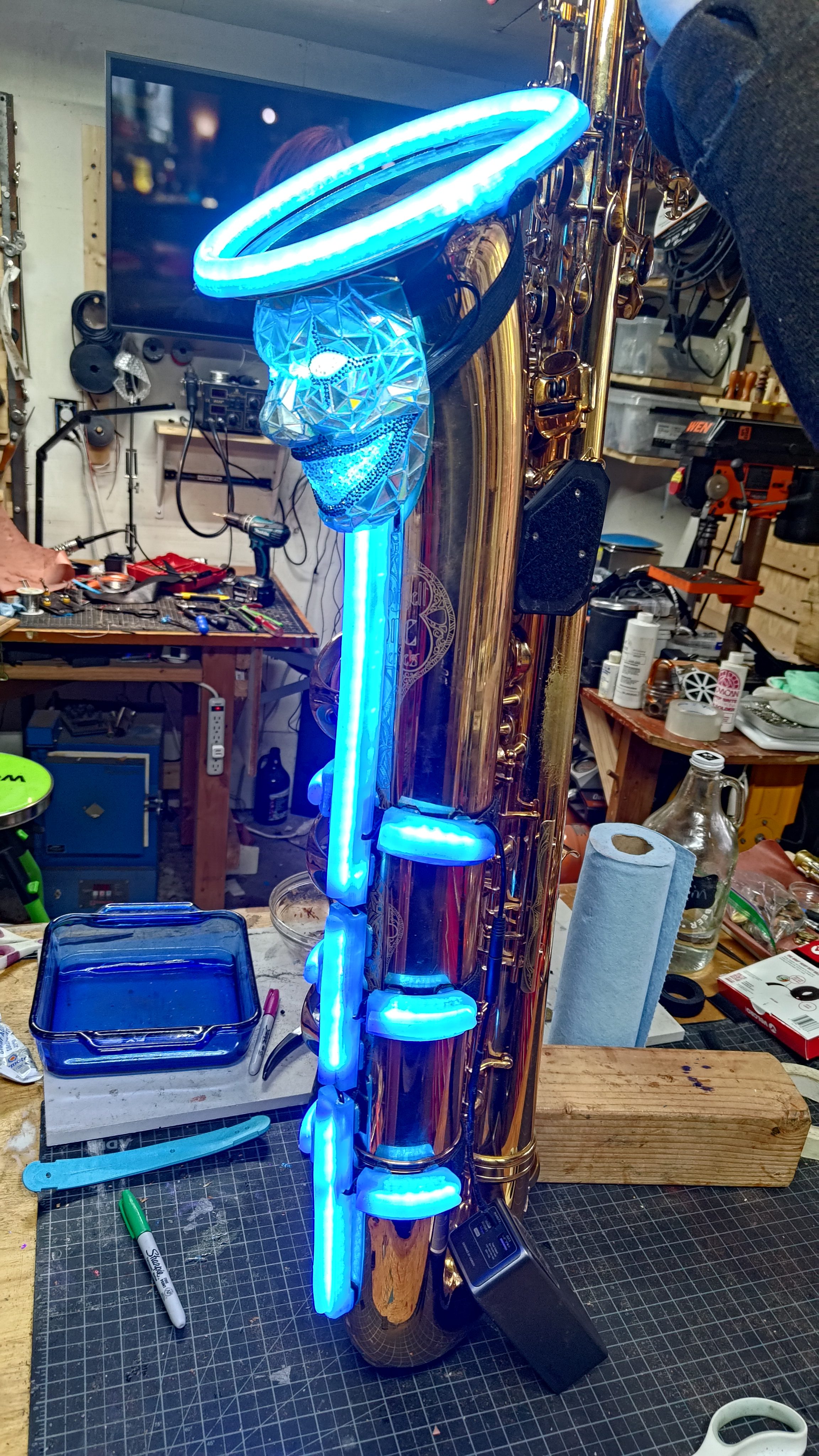A saxophone standing in the workshop with a blue halo ring and lit coils.