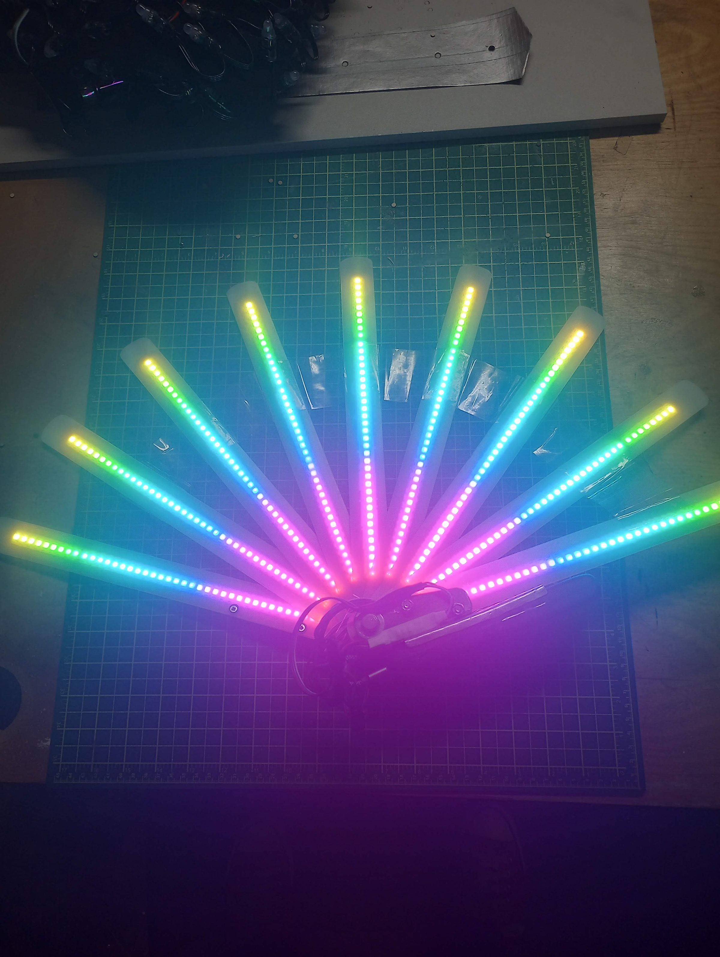 The LED hand fan opened flat, its blades lit in rainbow colour.