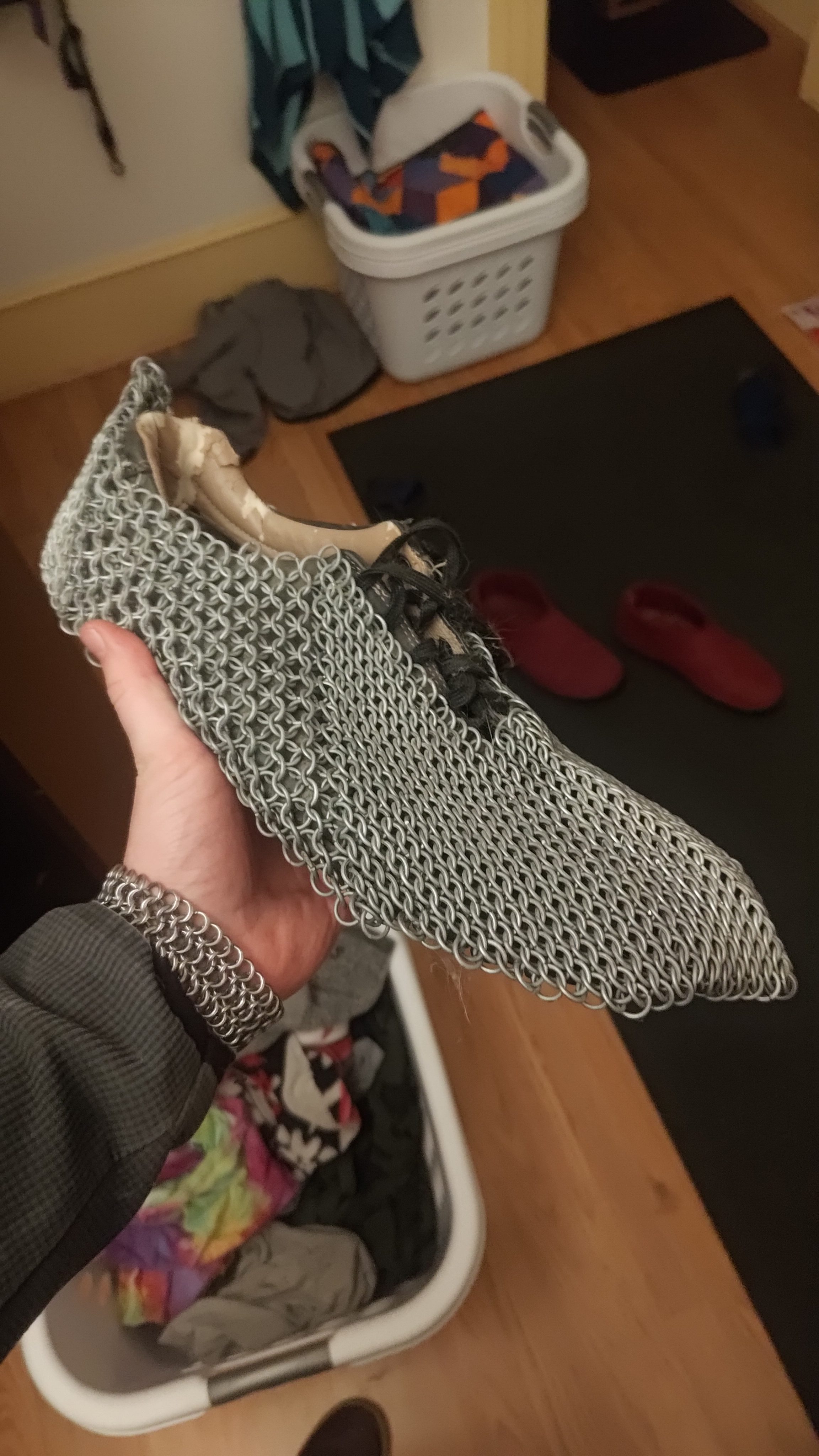 A chainmaille slipper held up in one hand.
