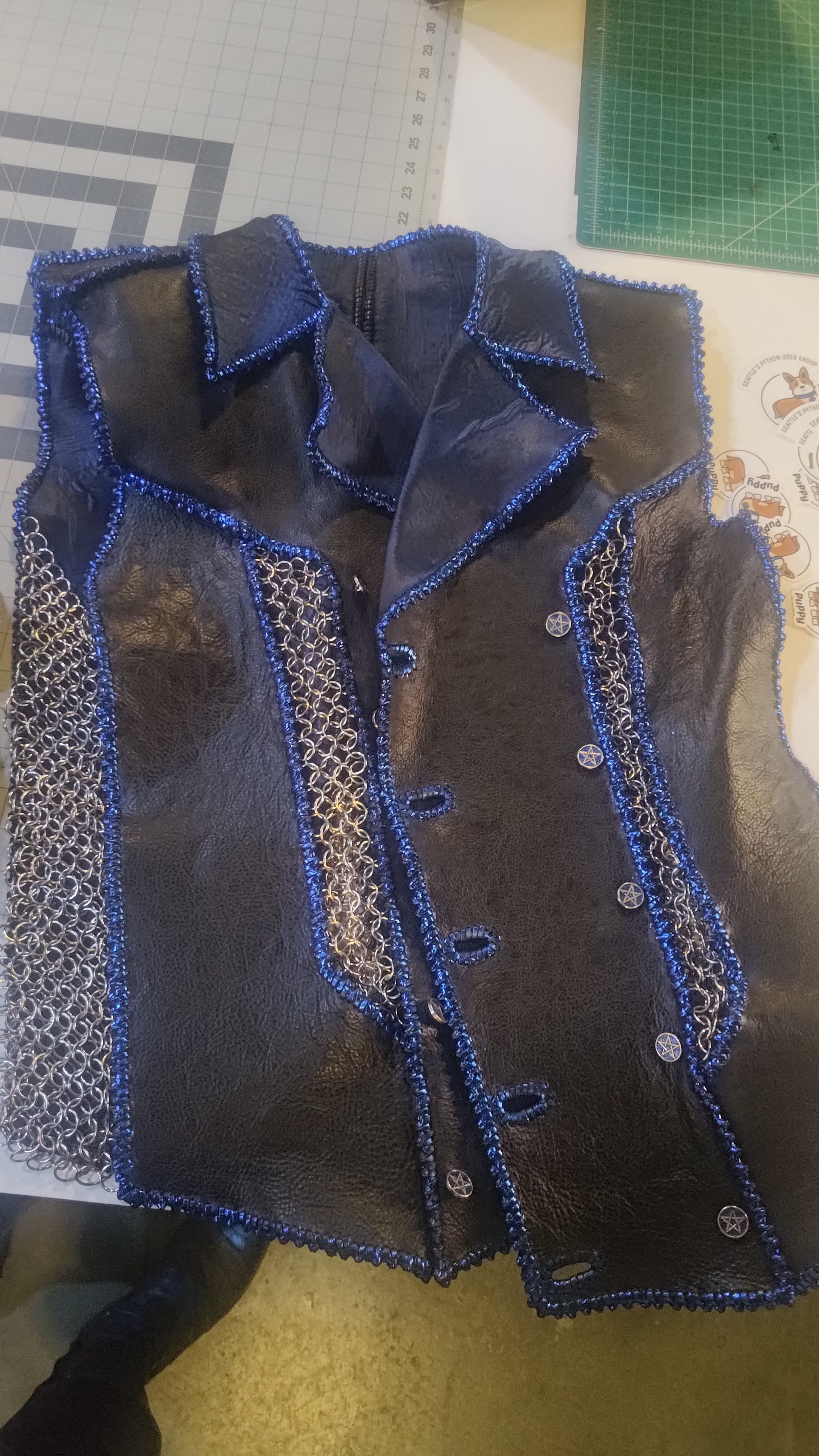A leather vest with chainmaille panels and blue trim, laid out flat.