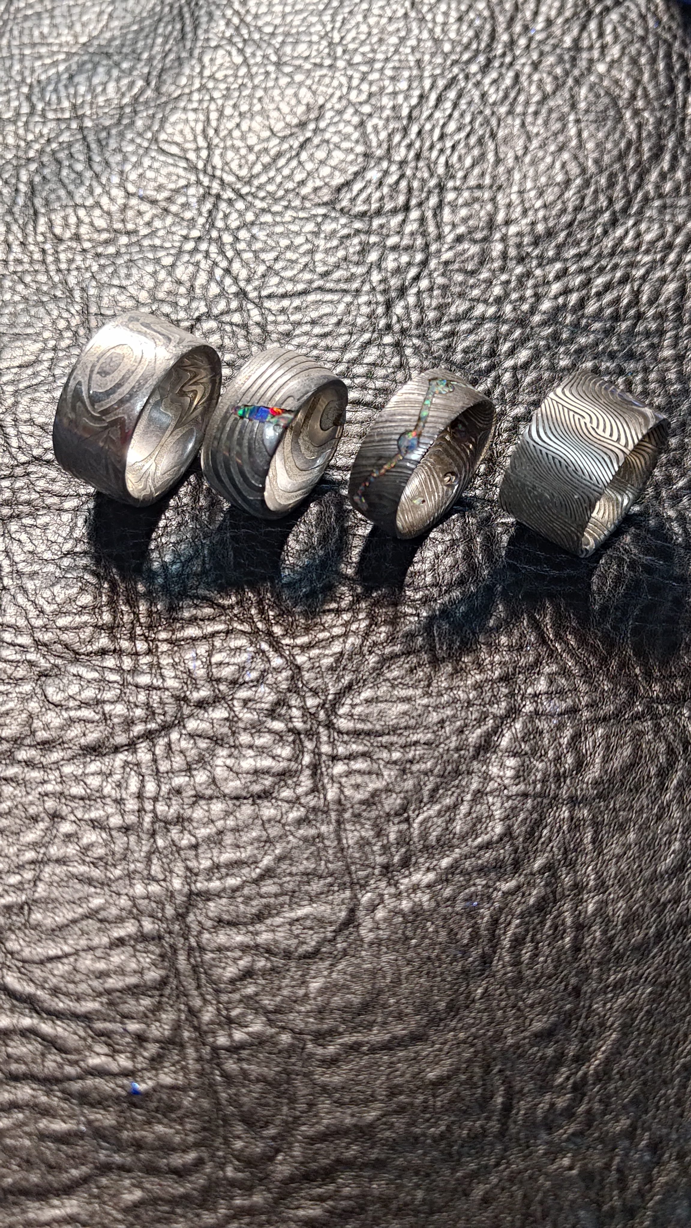 Five damascus steel rings lined up on black leather.