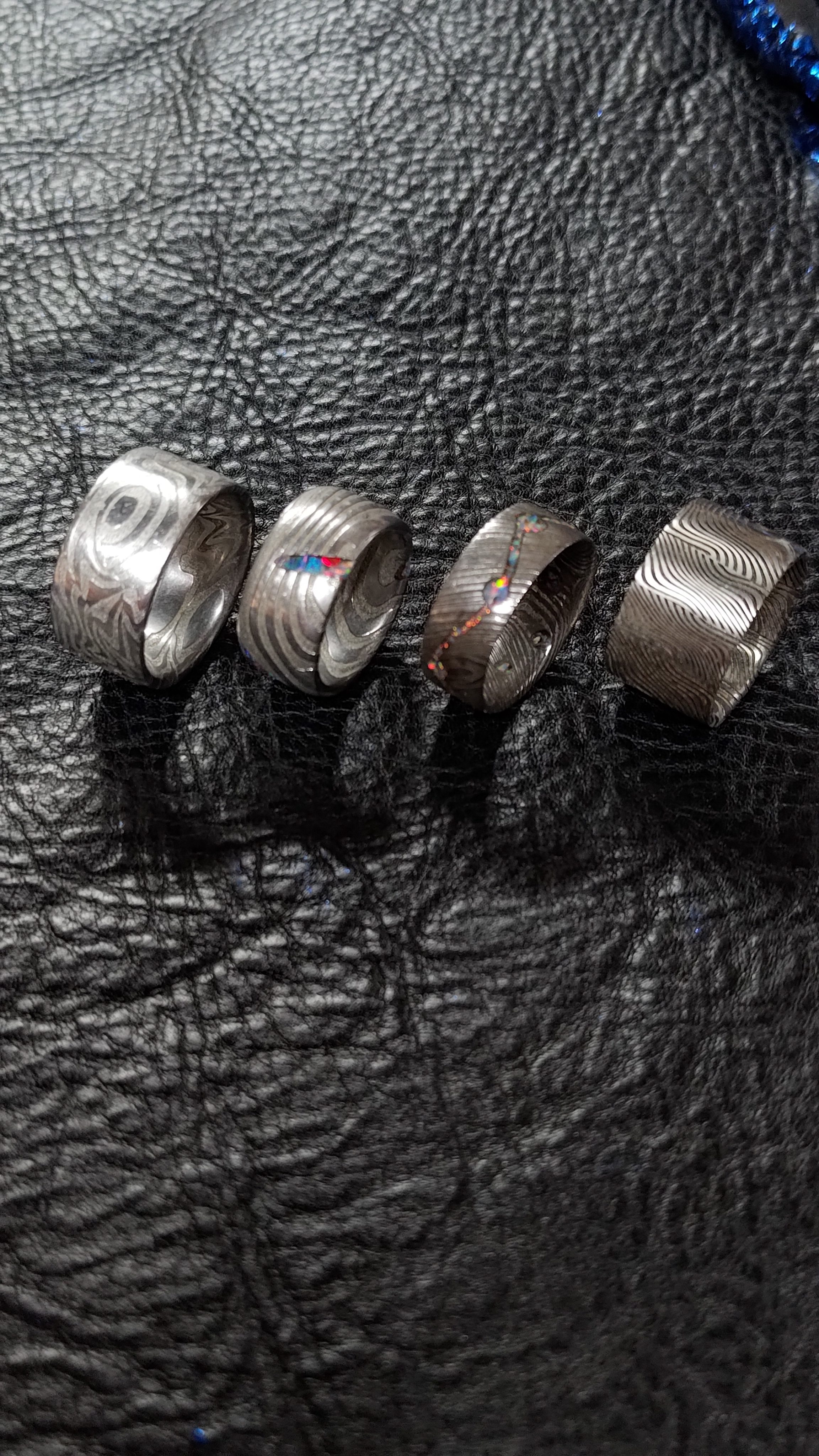 Five damascus rings on black leather, seen from a lower angle.