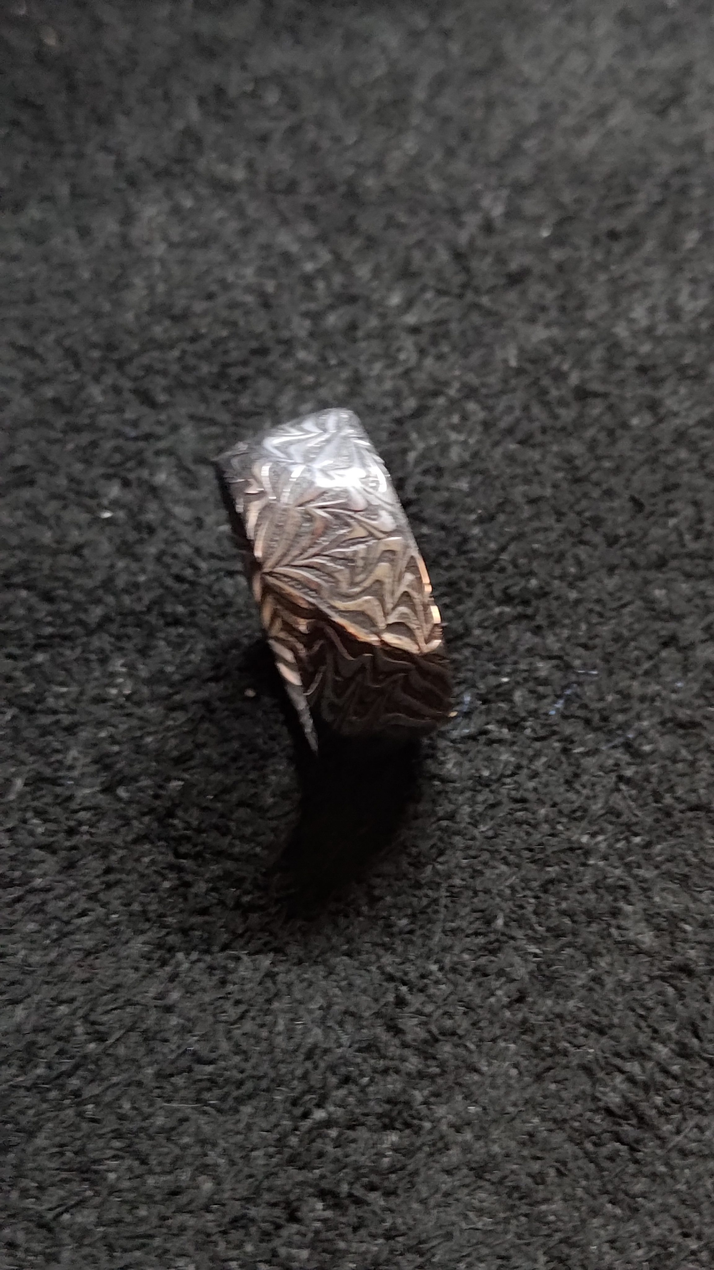 A damascus ring standing upright on a dark textured surface.