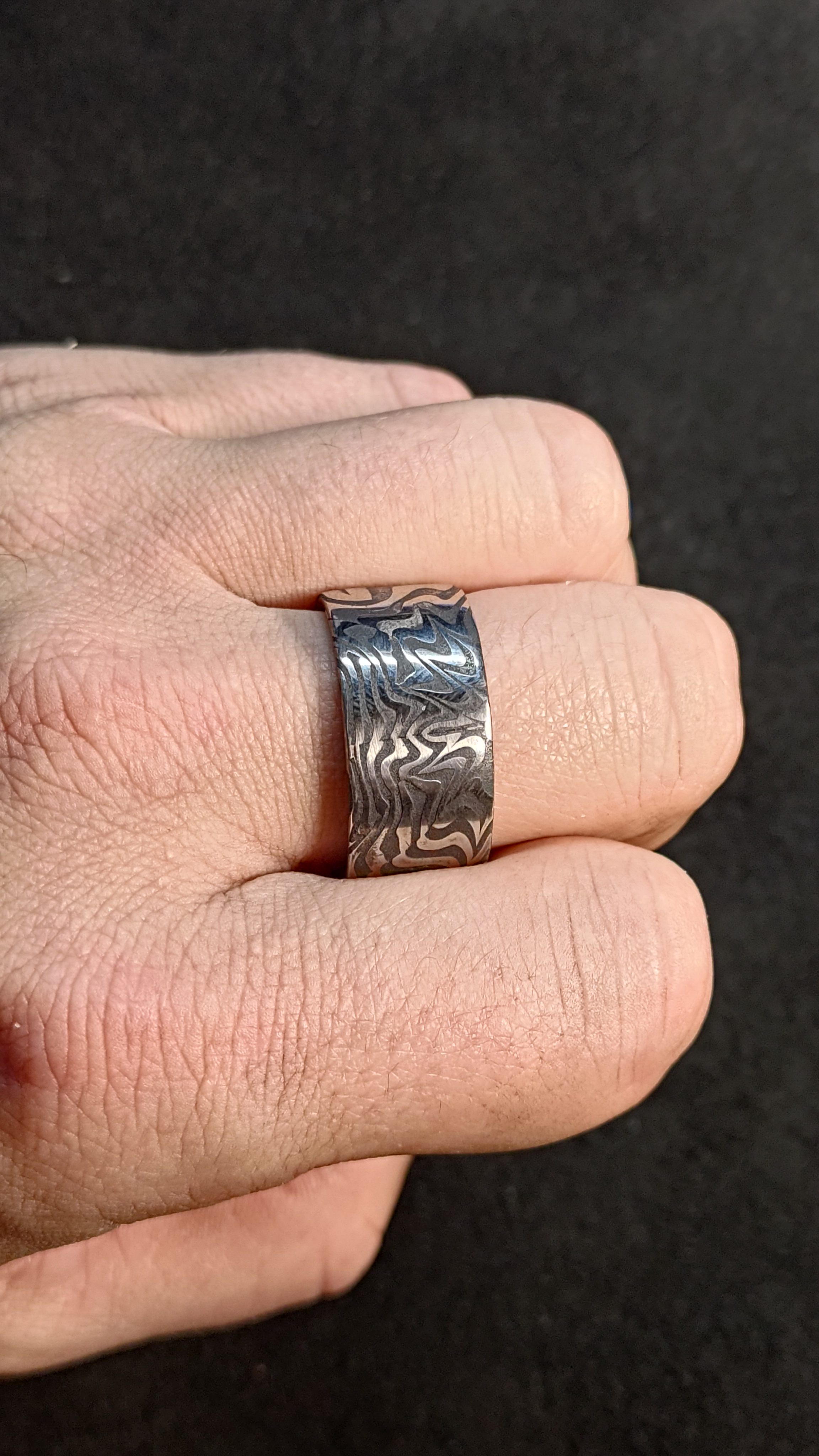 A damascus steel ring worn on a hand.