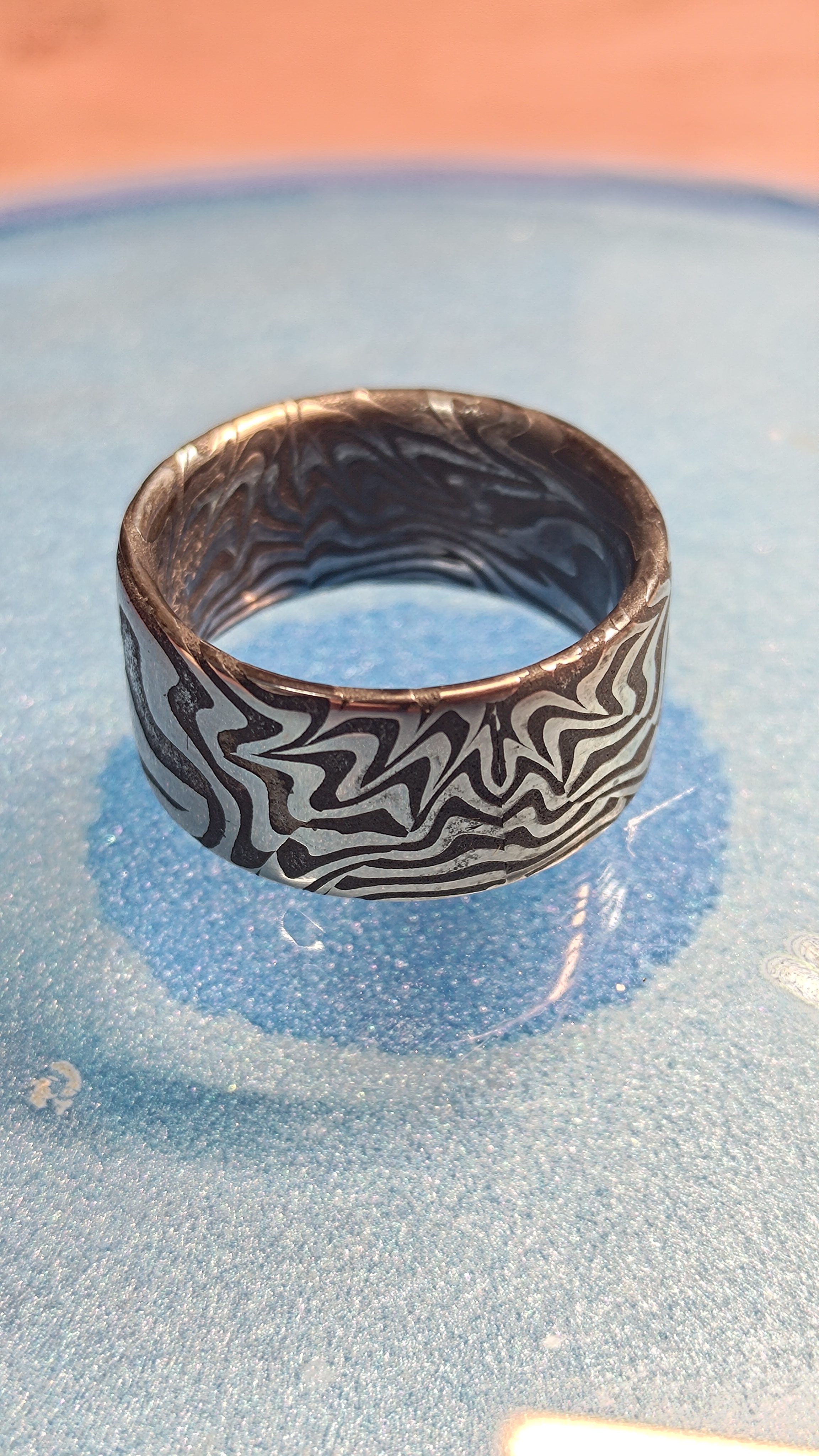 A damascus ring resting on a blue dish, its swirled pattern in high contrast.