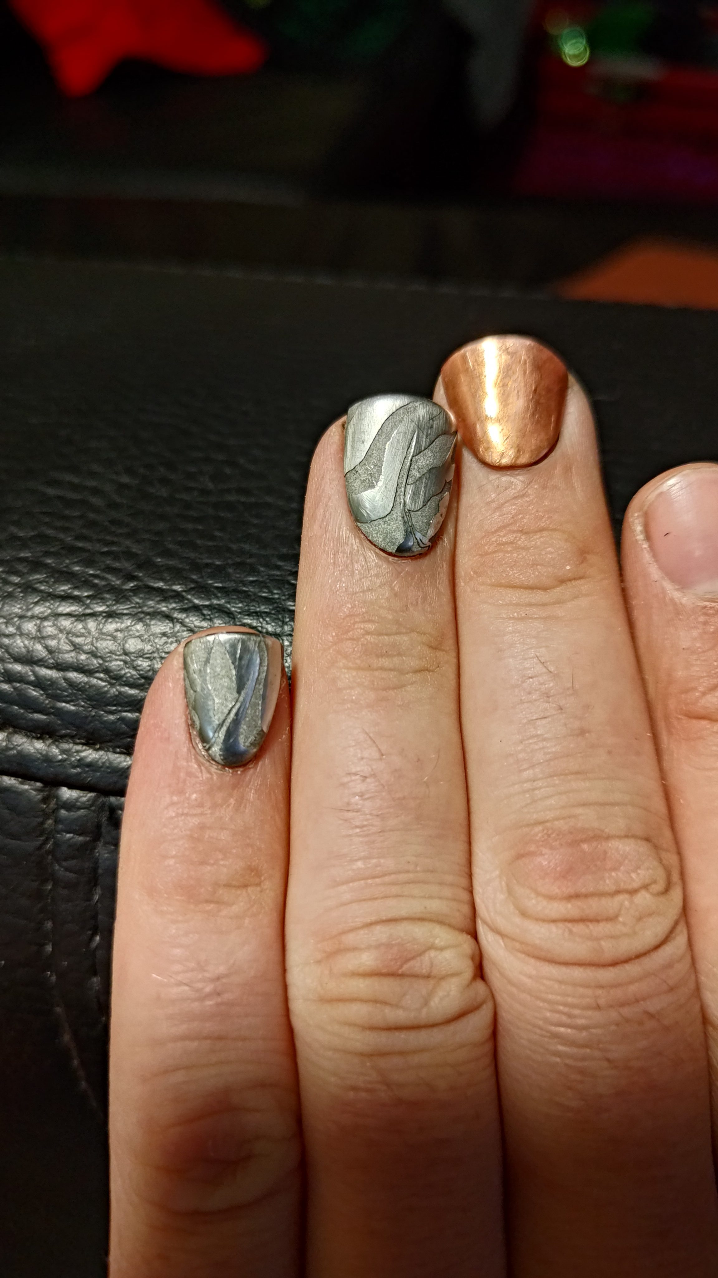 Close-up of damascus and copper press-on nails against black leather.