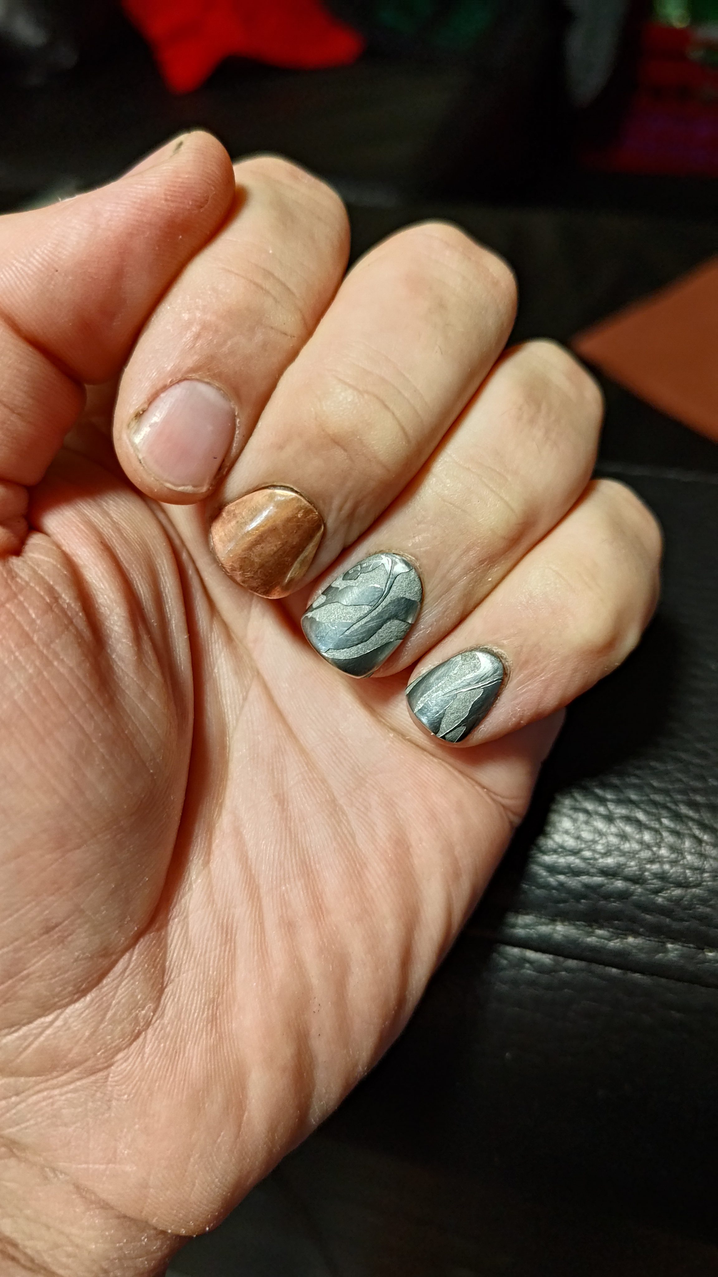 A curled hand showing copper and damascus press-on nails.