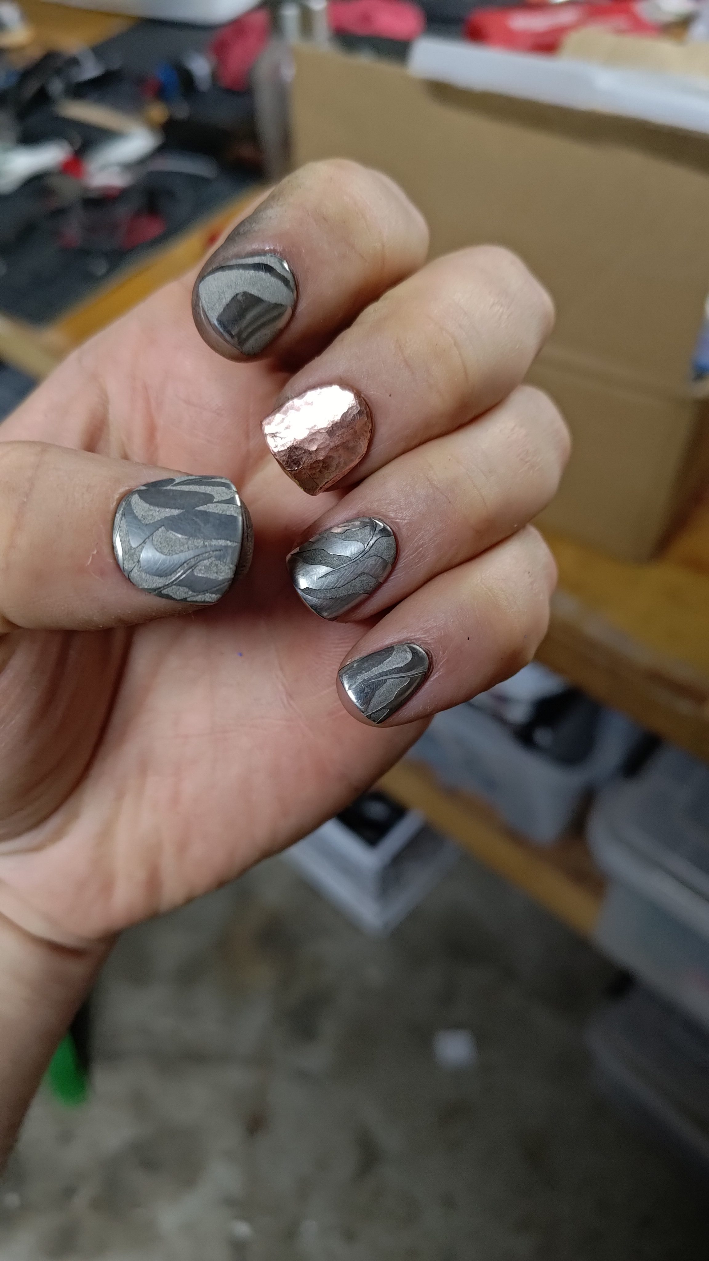 Damascus and copper press-on nails photographed in the workshop.