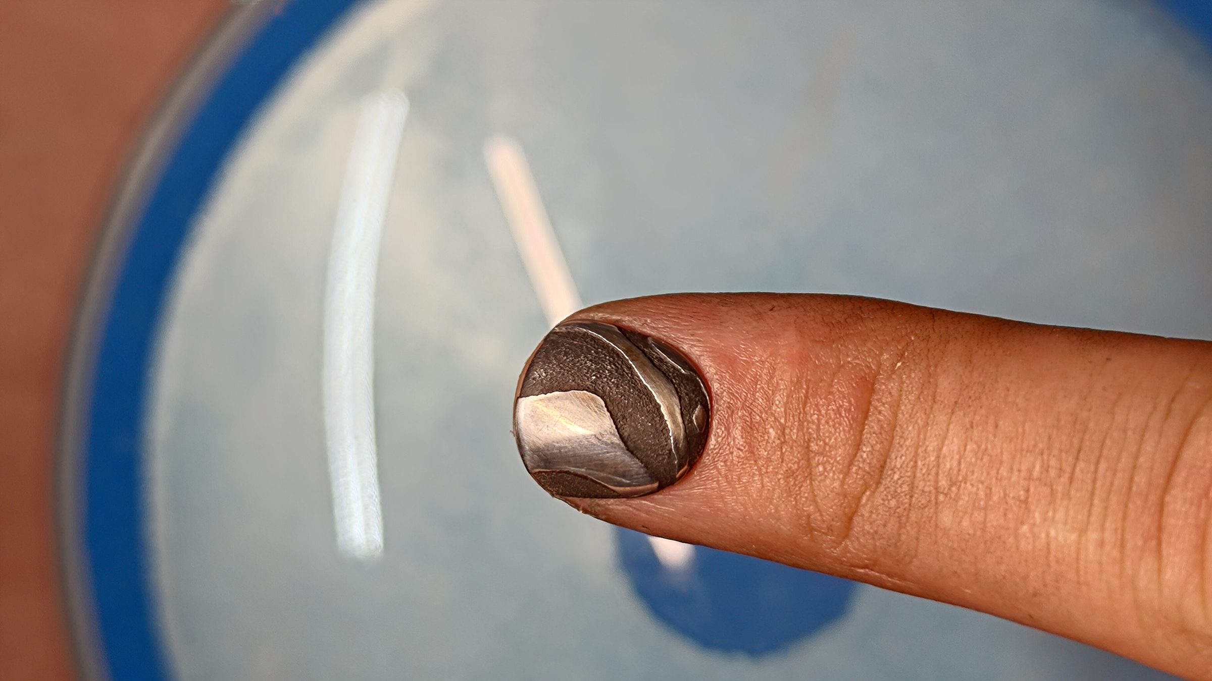 A single copper and damascus nail on a fingertip above a blue dish.
