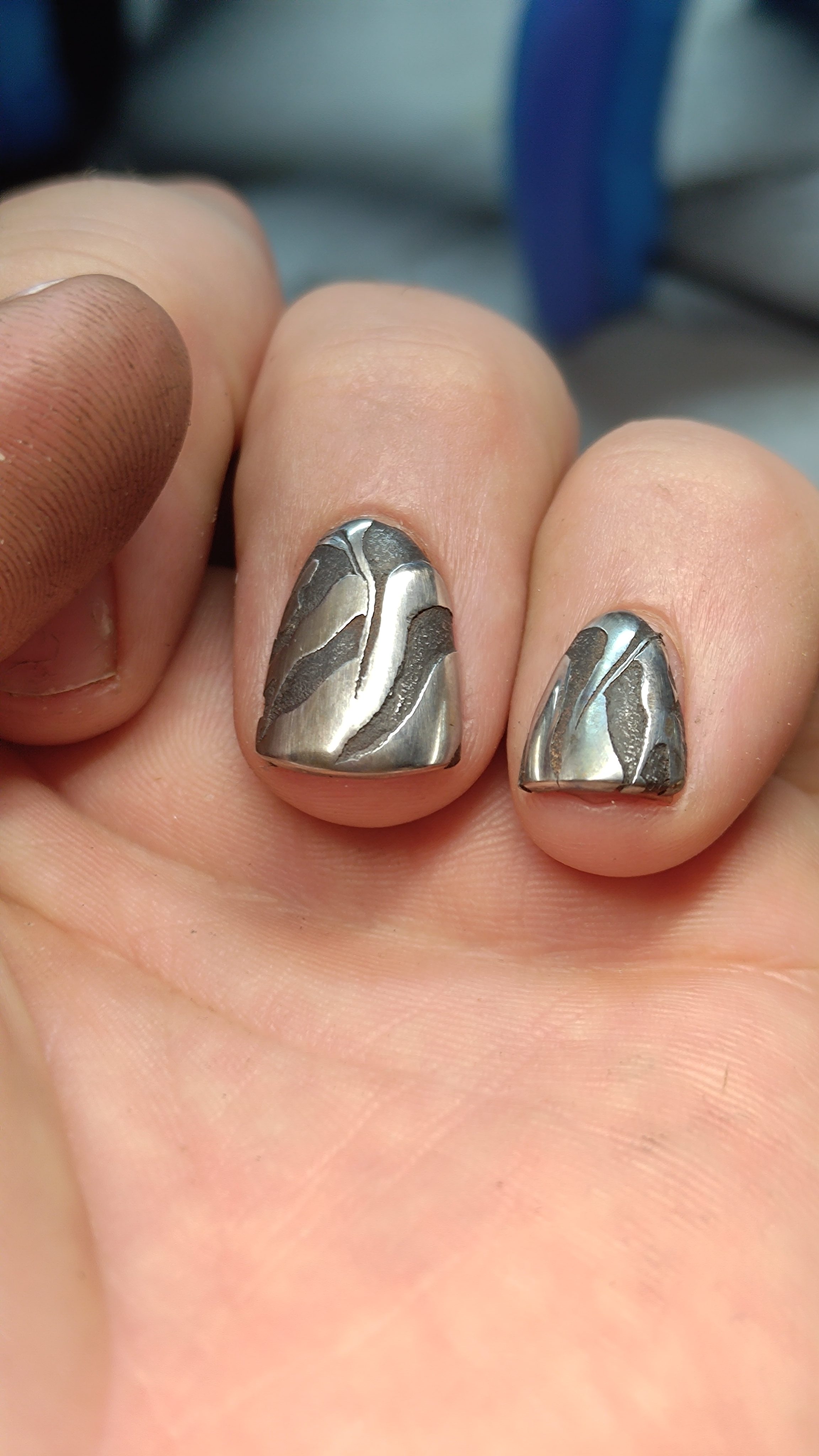 Two damascus-patterned nails seen close up on a hand.