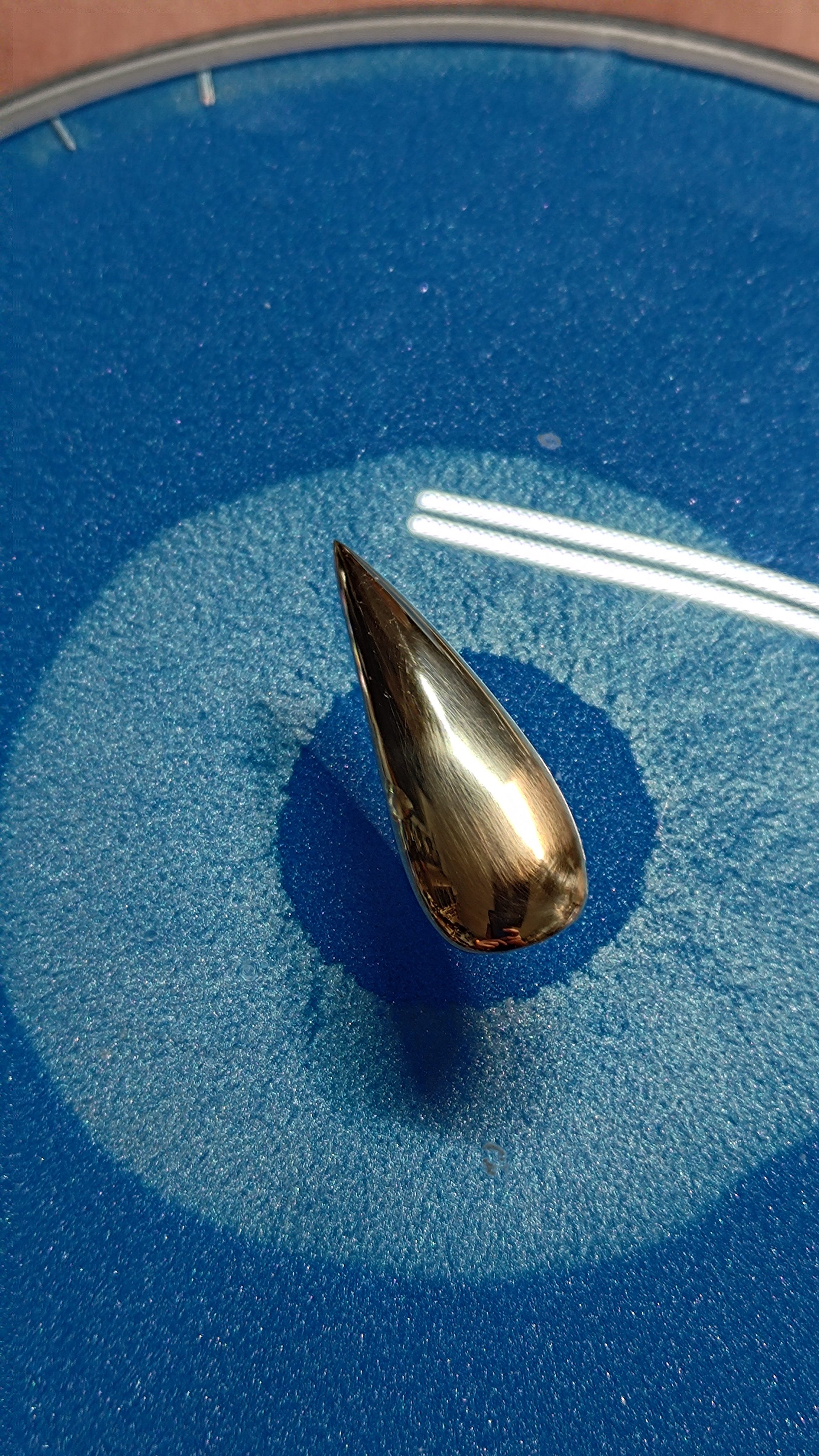 A single polished copper nail resting on blue abrasive.