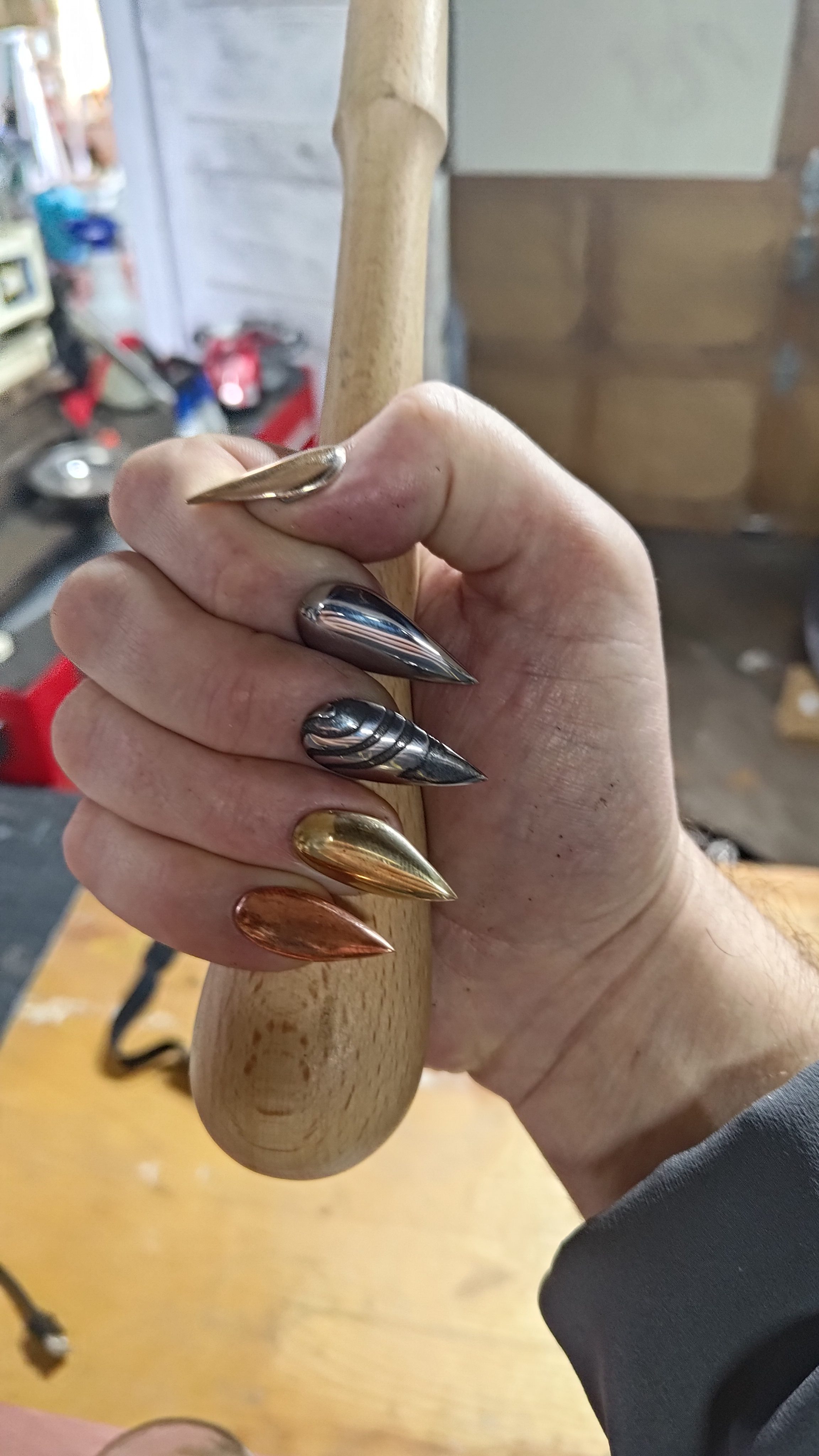 A hand with long damascus nails gripping a wooden handle in the workshop.