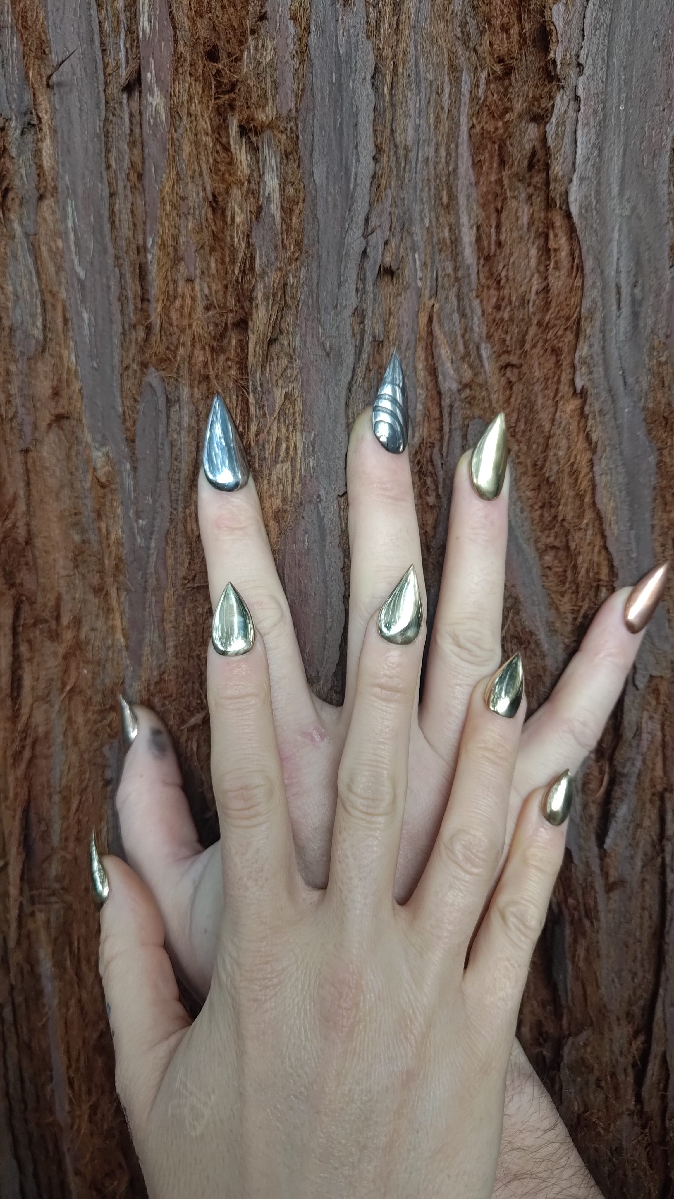 Hands with long polished silver nails spread against tree bark.