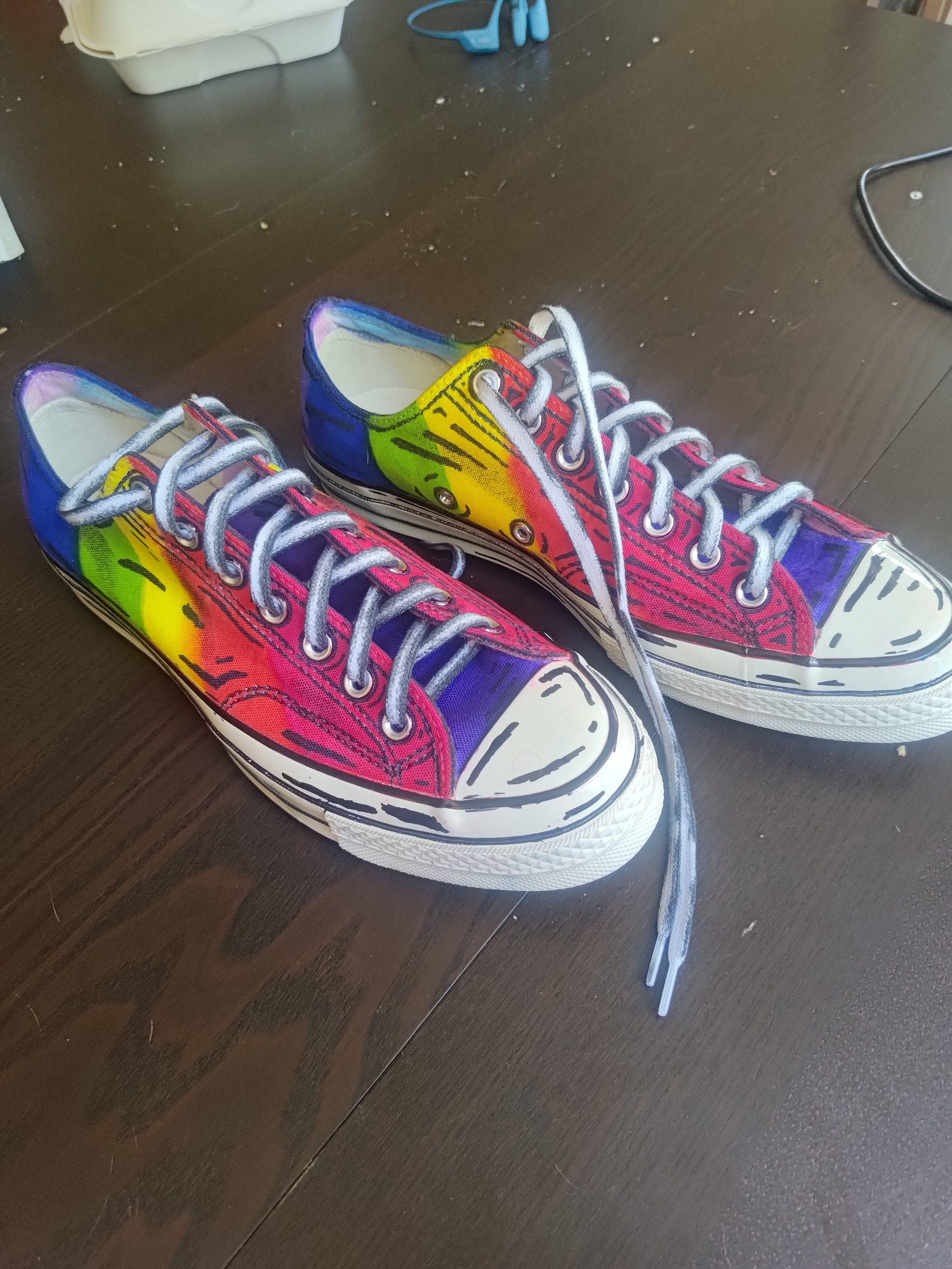 A pair of hand-painted rainbow sneakers on a table.