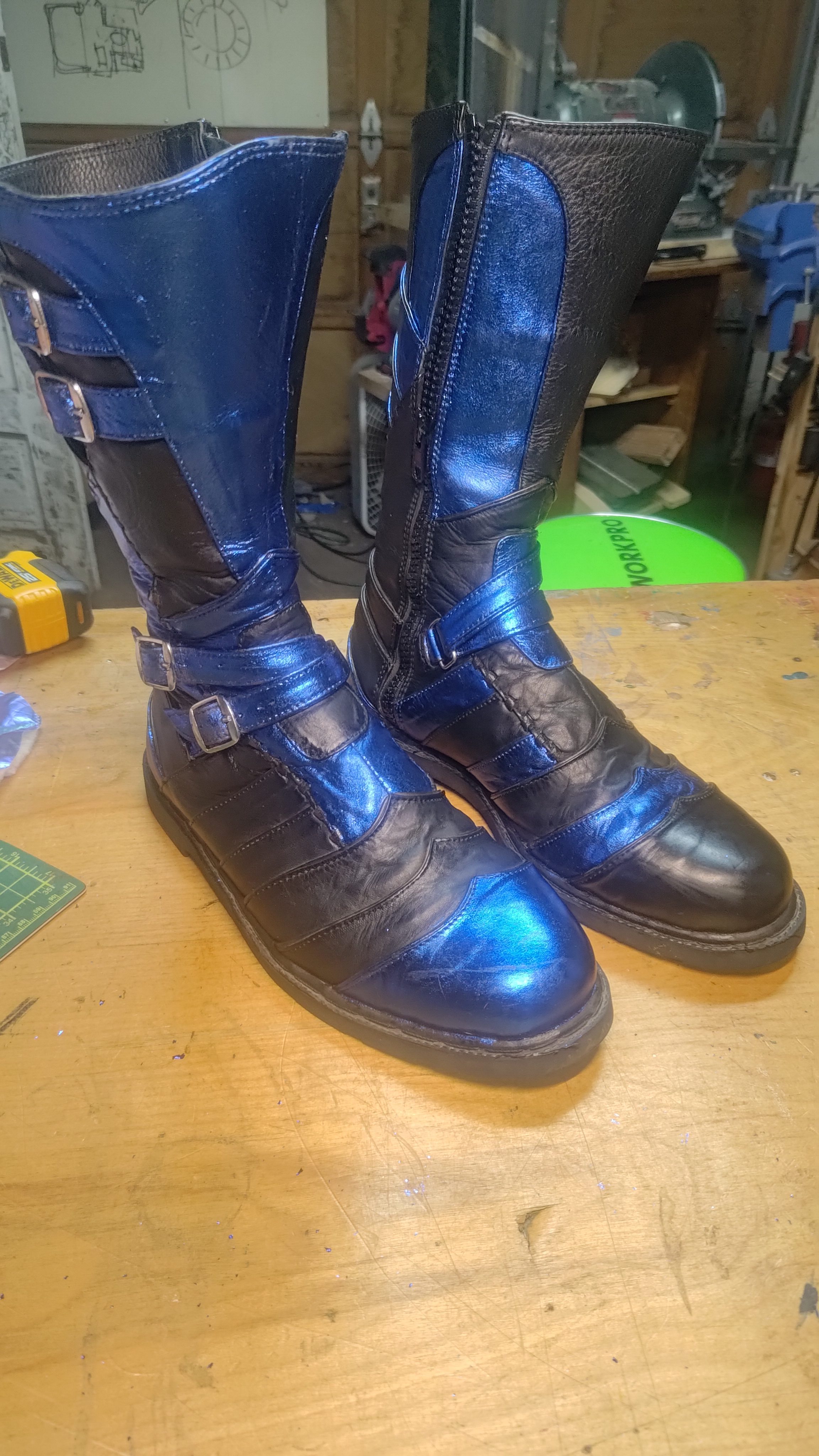 Hand-made black and blue leather boots on a workbench.